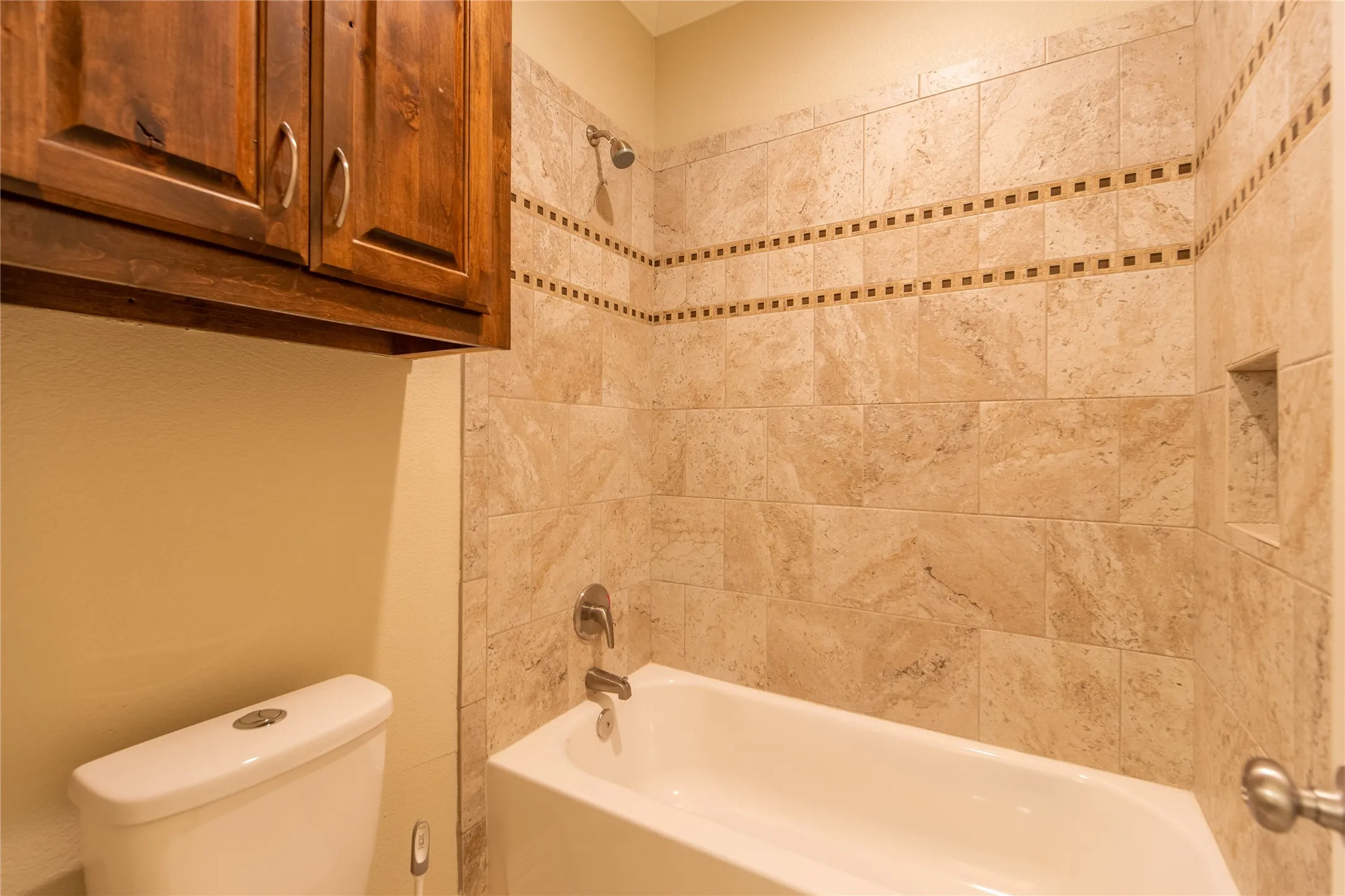 Spa-inspired bathroom featuring travertine tile walls with decorative stone-pattern border detailing, a ceramic soaking tub with chrome fixtures, and warm neutral finishes throughout