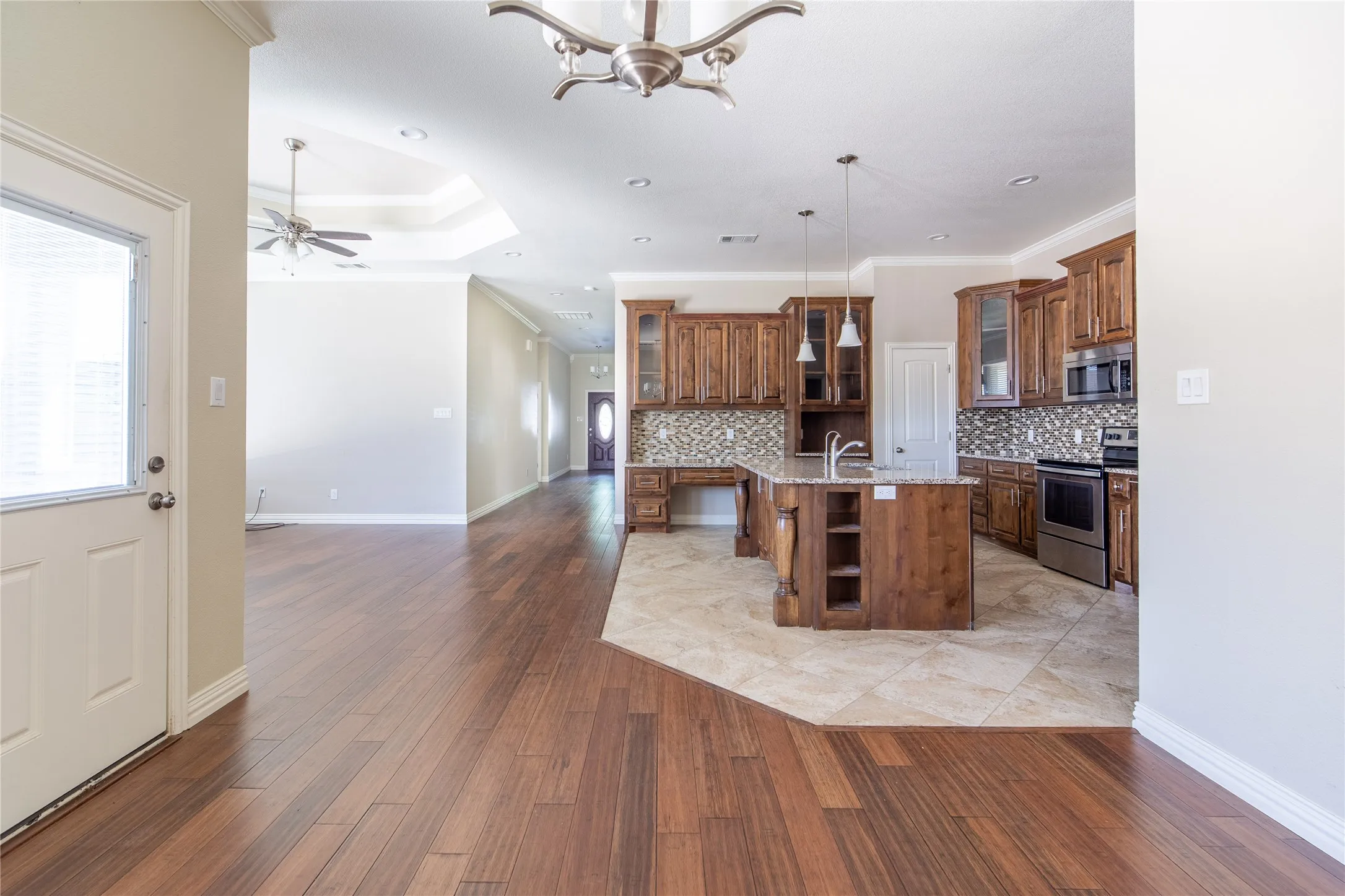 Wood-finish flooring, recessed lighting, tray ceiling, kitchen island with built-in storage, and stainless steel appliances