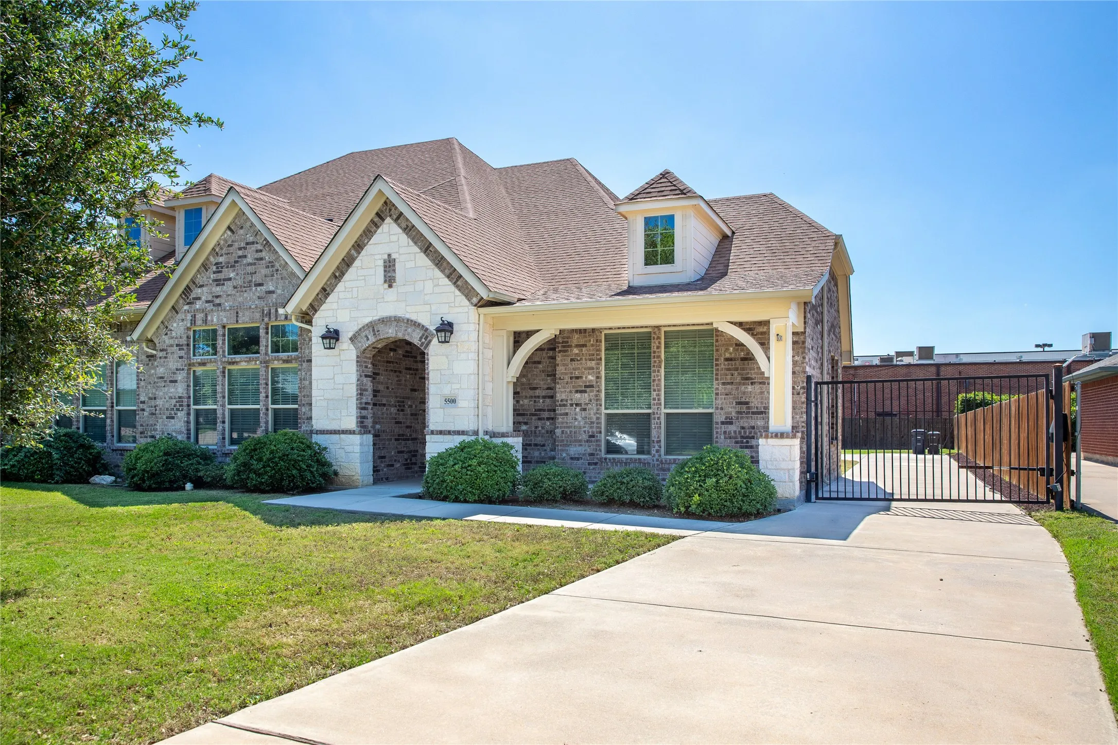 Elegant two-story residence featuring a mixed-material exterior of cream-colored stucco and stone accents, arched entryway with wood-finish doors, and a complex roofline with multiple gables and dormers