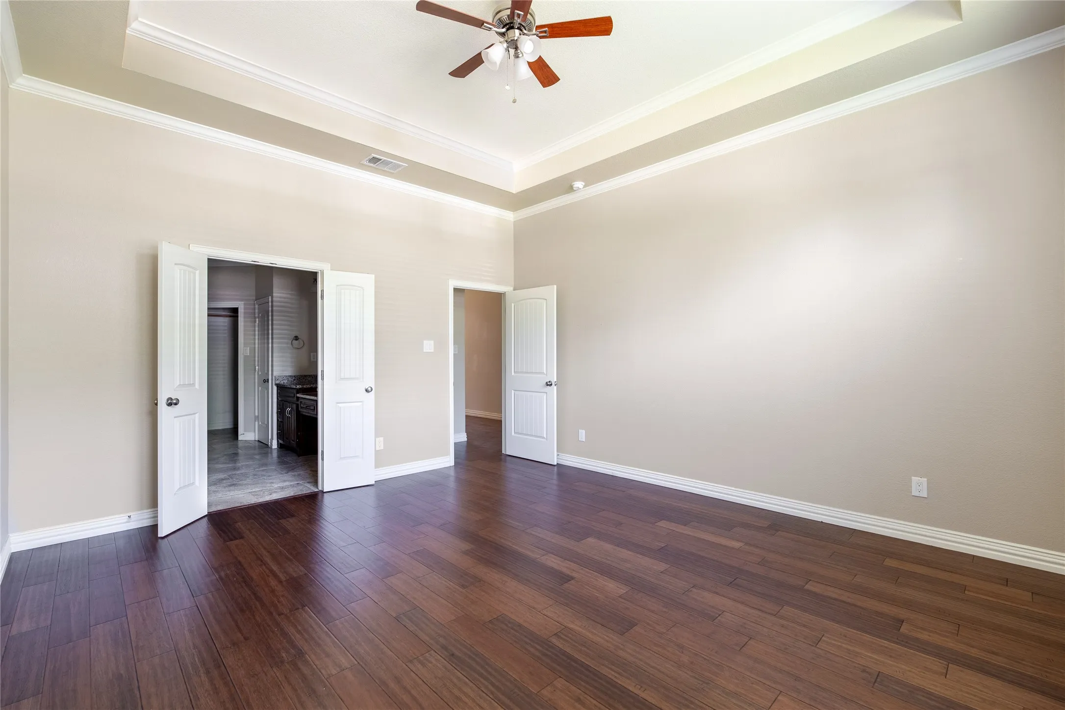 Tray ceiling with crown molding, wood-finish flooring, and ceiling fan