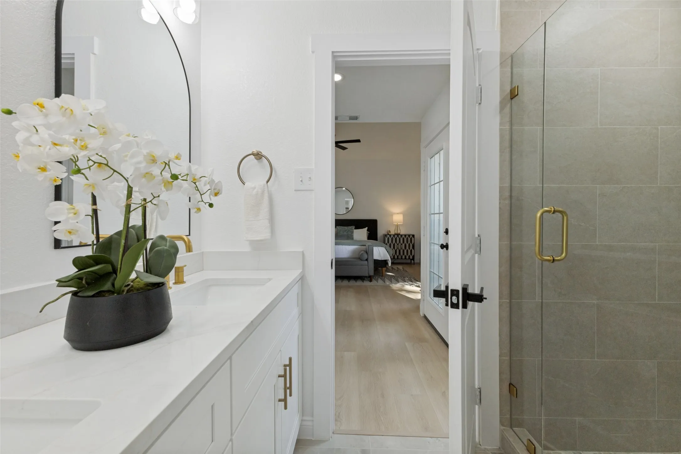 Primary bath with a double vanity, gold-tone hardware, an expansive mirror, and a glass-enclosed shower