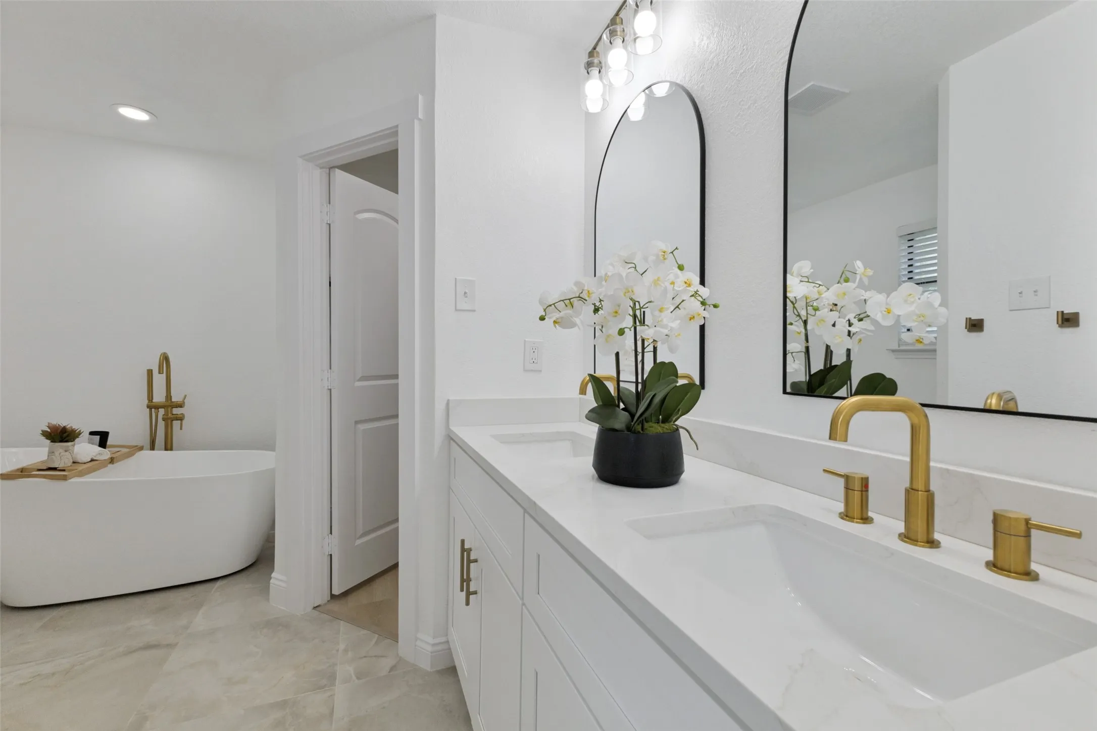 Primary bath with a dual vanity, white shaker-style cabinetry, quartz countertop, and gold-finish fixtures