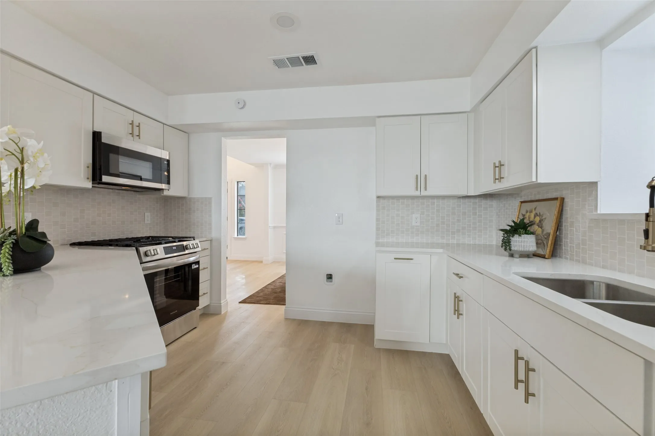 White cabinetry with gold-tone hardware, luxury vinyl plank flooring, stainless steel appliances, quartz countertops, and a mosaic tile backsplash