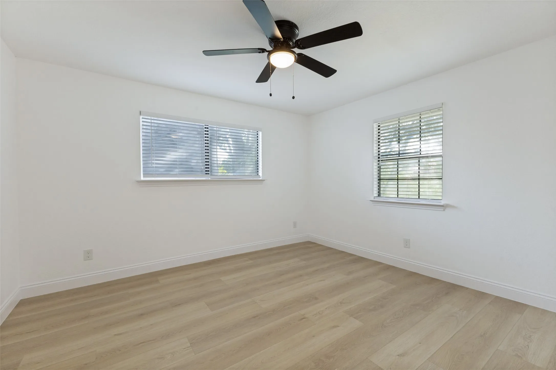 Light-filled upstairs bedroom featuring two windows with blinds, luxury vinyl plank flooring, a ceiling fan with integrated lighting, and crisp white walls