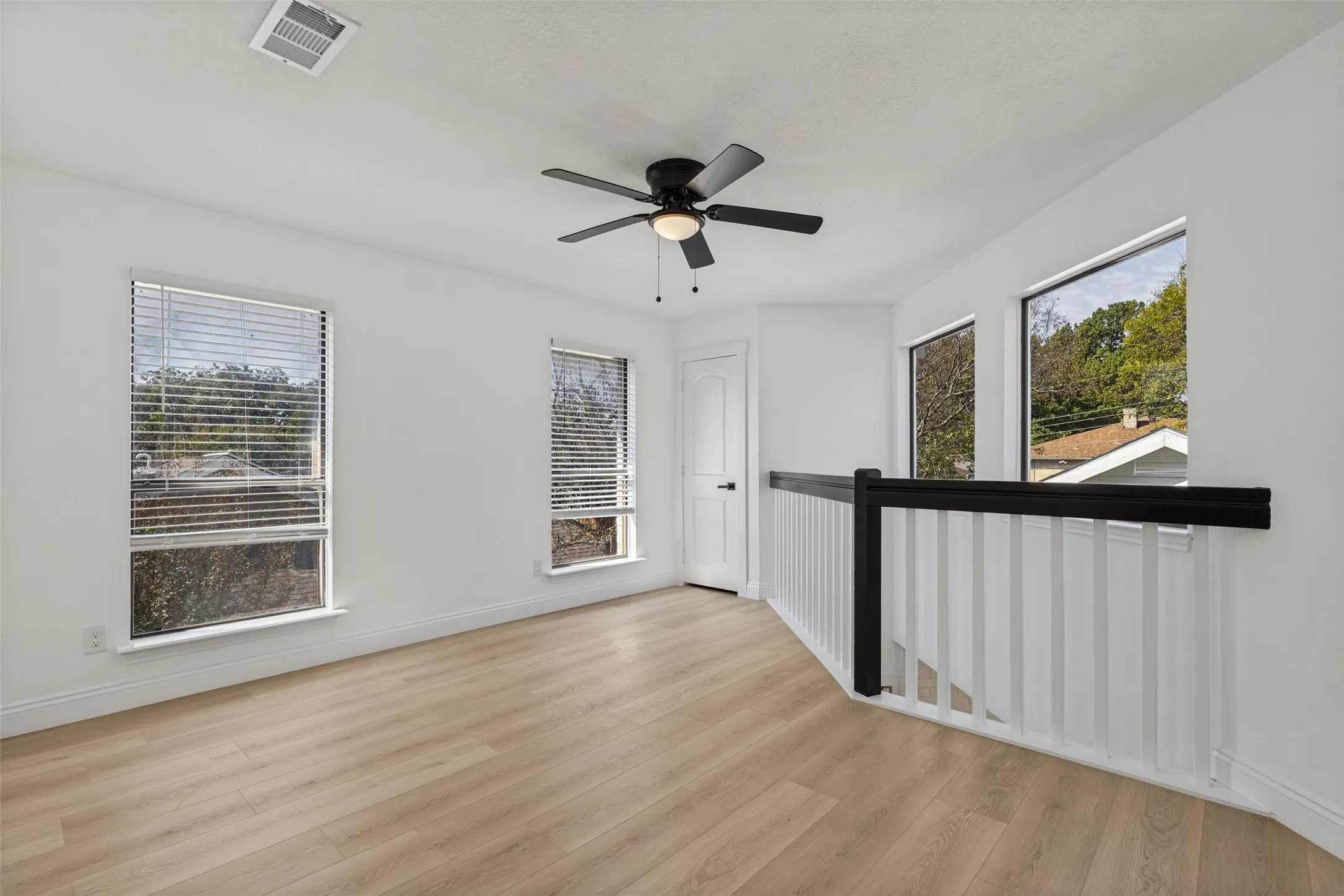 Upstairs loft and game room with luxury vinyl plank flooring, multiple windows, a ceiling fan, and a black and white railing