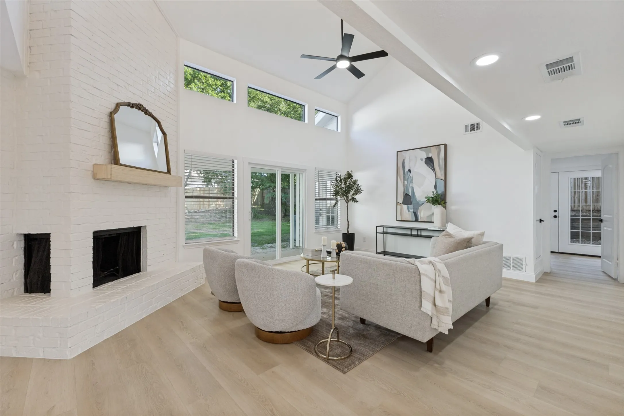 Vaulted ceiling with an integrated ceiling fan, white brick fireplace, luxury vinyl plank flooring, transom windows, and sliding glass doors