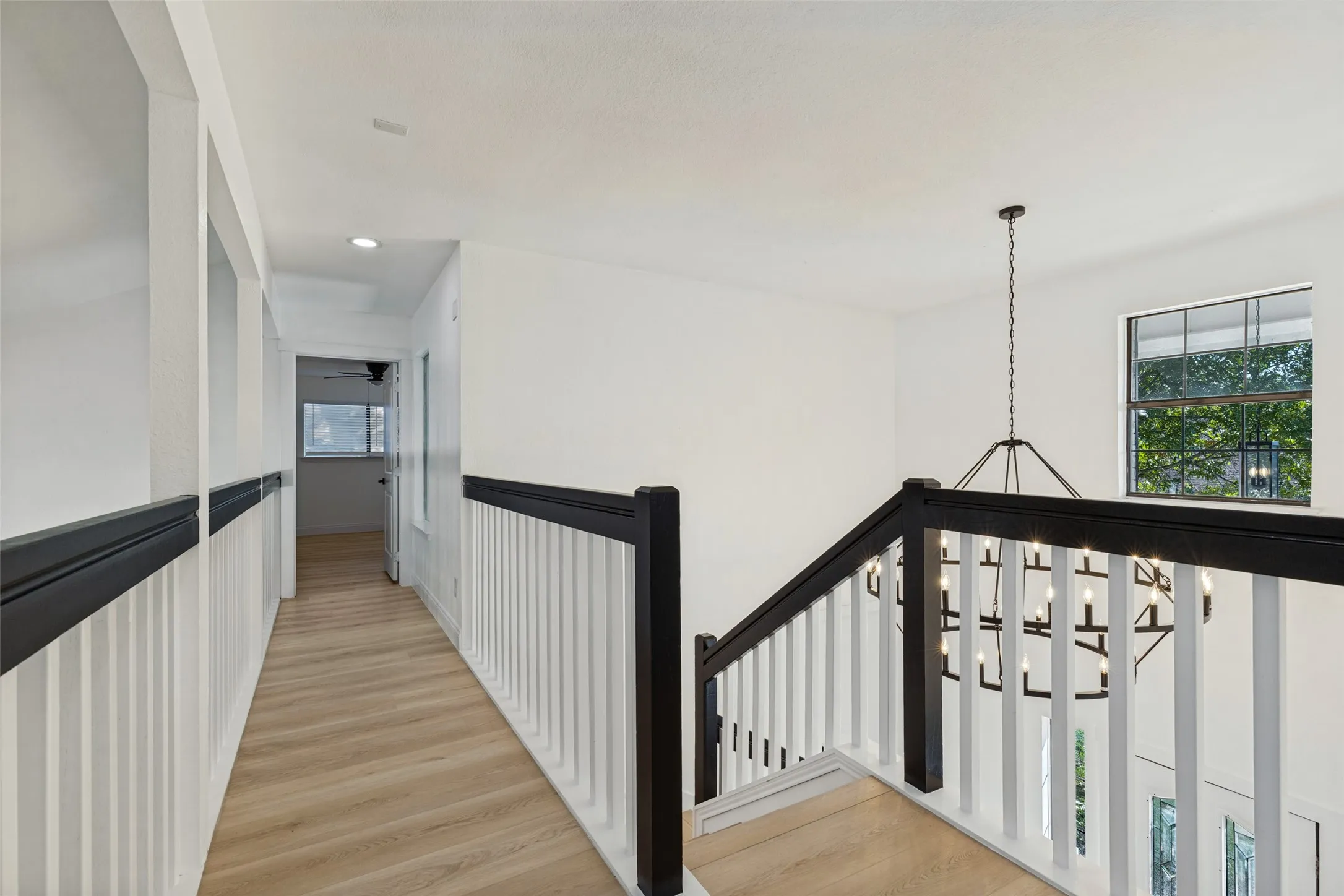 Upstairs hallway with luxury vinyl plank flooring, white walls, and a black and white stair railing