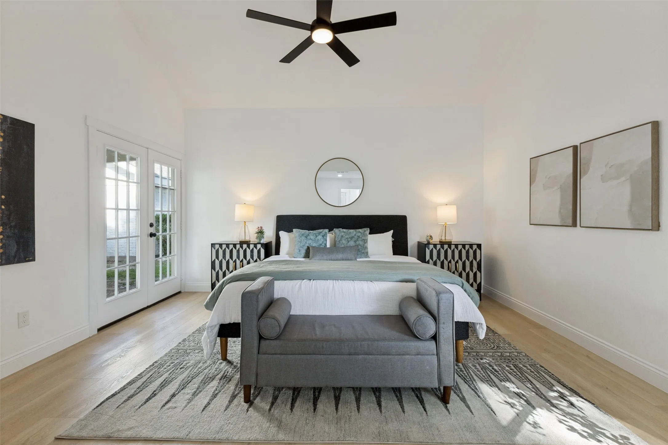 First-floor primary bedroom with a vaulted ceiling, luxury vinyl plank flooring, ceiling fan, and French doors