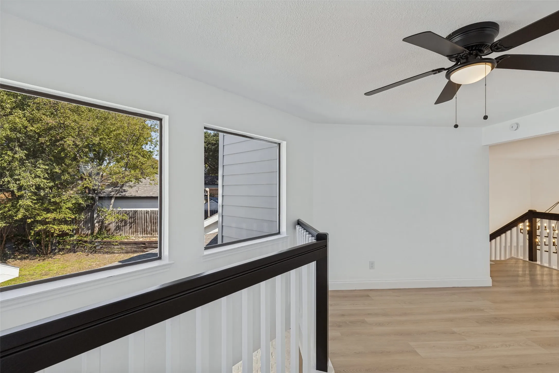 Upstairs loft with recessed lighting, luxury vinyl plank flooring, a black ceiling fan with integrated lighting, and a black and white railing