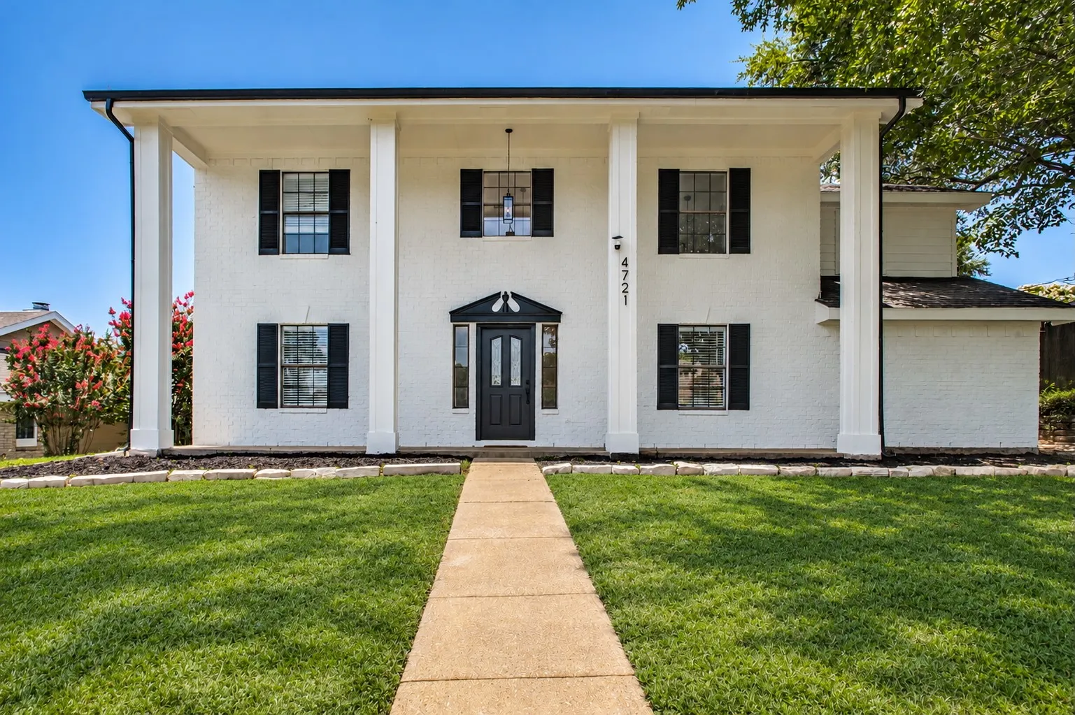 White brick colonial exterior with prominent architectural columns, a black paneled front door, and symmetrical windows with black shutters