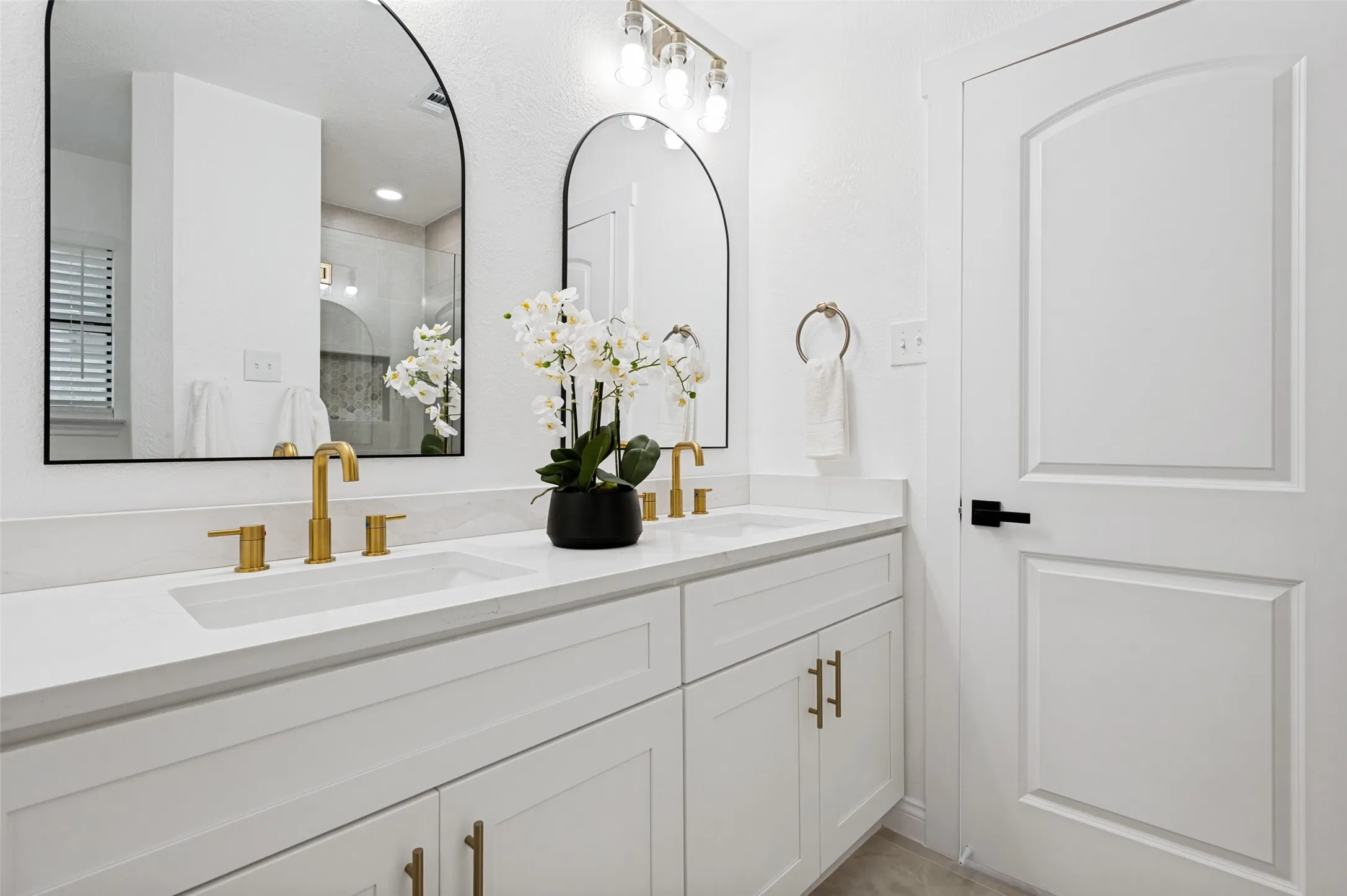 Primary bath with dual arched mirrors, a white shaker-style double vanity, and gold-finish hardware