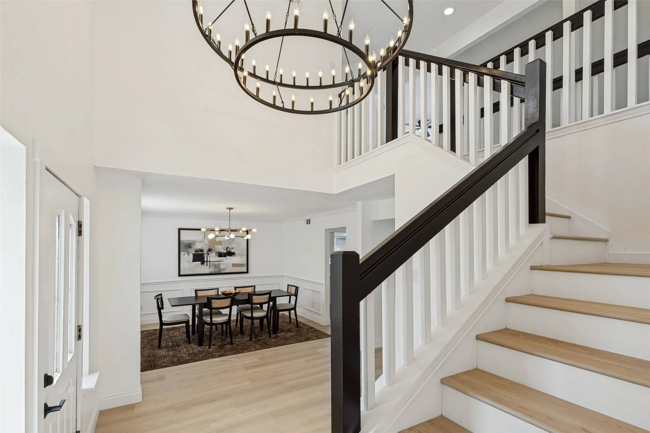 Double-height foyer with a circular wrought iron chandelier, luxury vinyl plank flooring, and a two-tone staircase featuring white risers and dark wood handrails