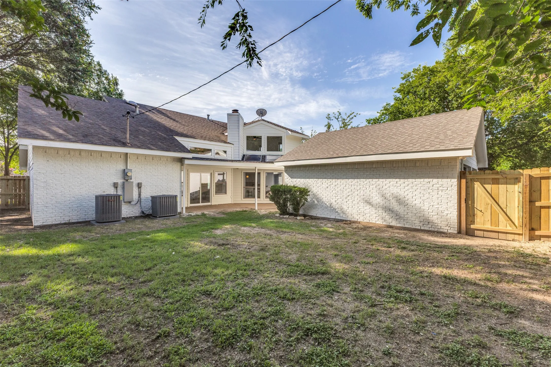 Large fenced backyard featuring a paved patio, white brick exterior, two HVAC units, a privacy fence, and mature trees