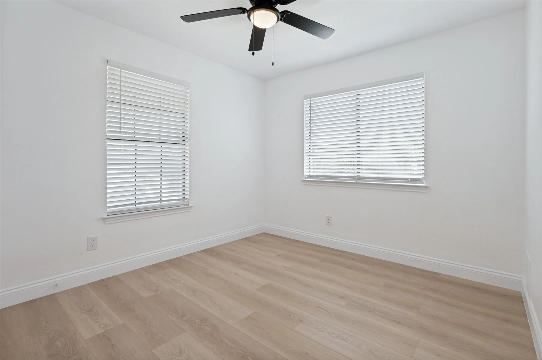 Upstairs bedroom with luxury vinyl plank flooring, white walls, two windows with blinds, and a ceiling fan with integrated lighting