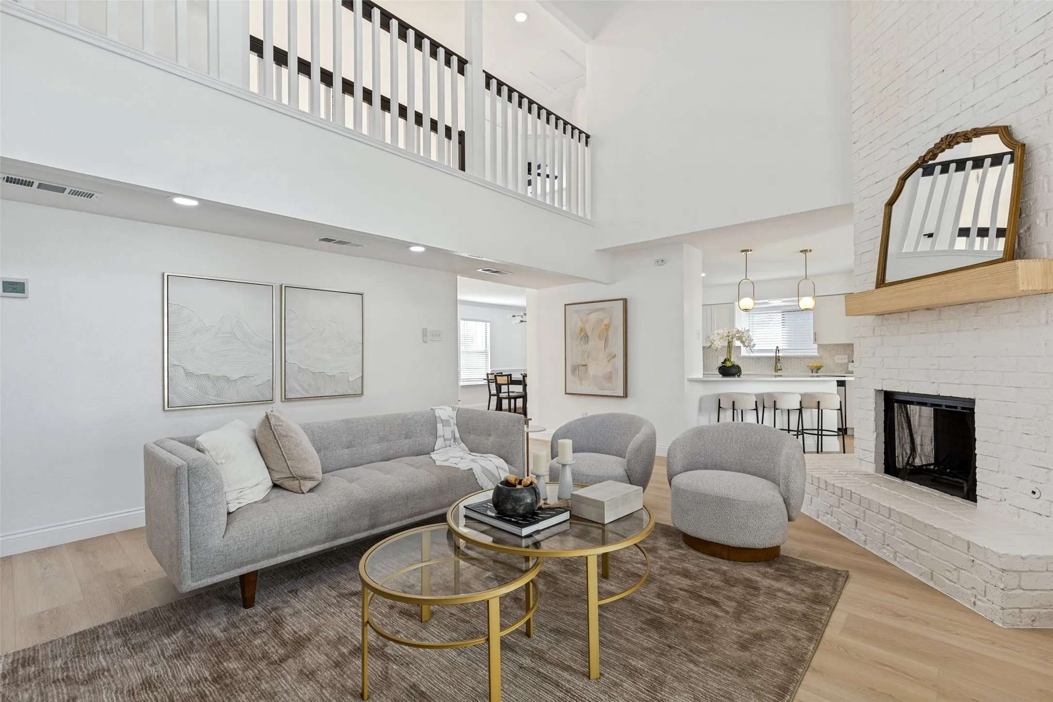 Vaulted living room with a white brick fireplace, luxury vinyl plank flooring, and an upper-level overlook with open railing