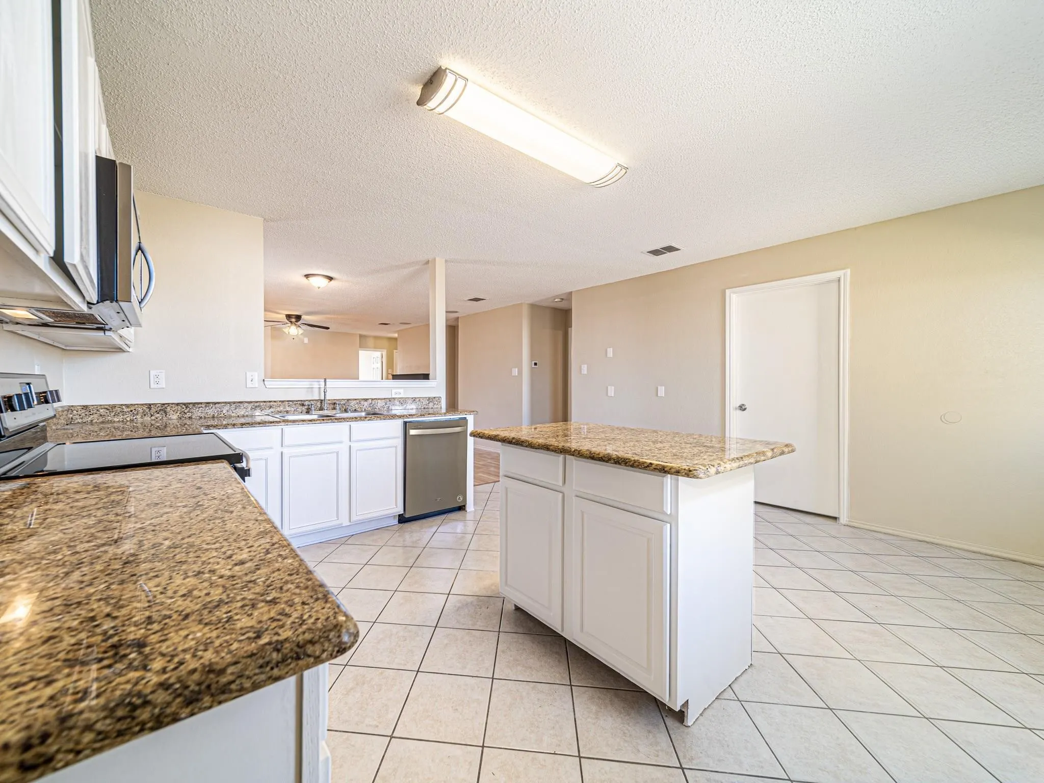 Kitchen featuring an electric range, stainless steel dishwasher, white cabinetry, and a center island with a granite countertop