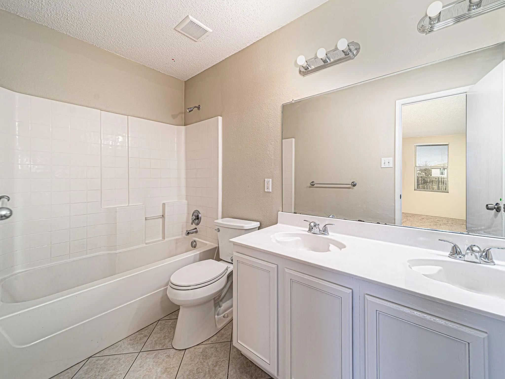 Bathroom featuring a dual vanity with integrated sinks, white cabinetry, a large mirror, a chrome-finish light fixture, and a tiled shower/tub combination