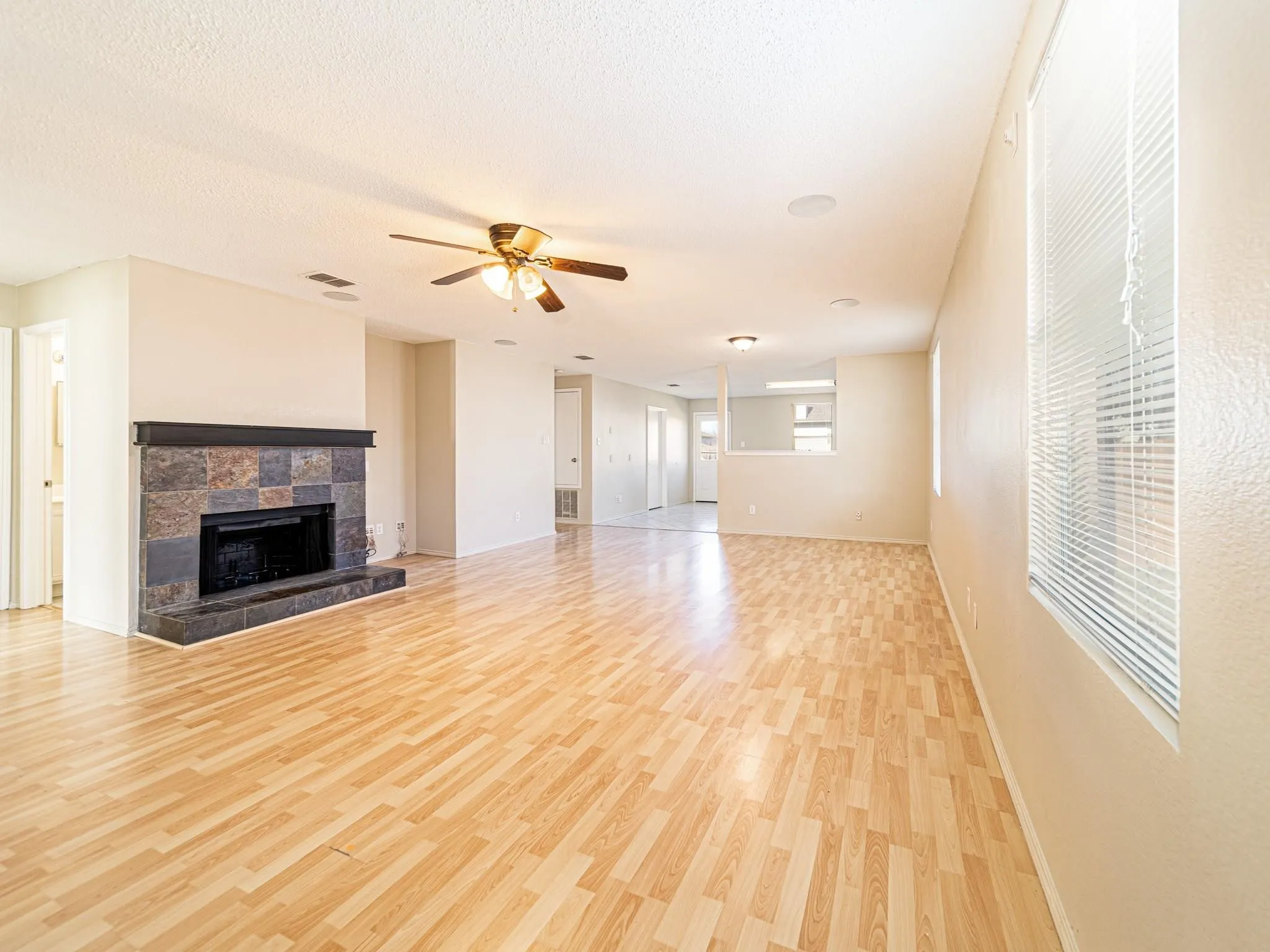 Living space featuring wood-finish flooring, a fireplace with a stone surround, multiple windows with blinds, a ceiling fan, and recessed lighting