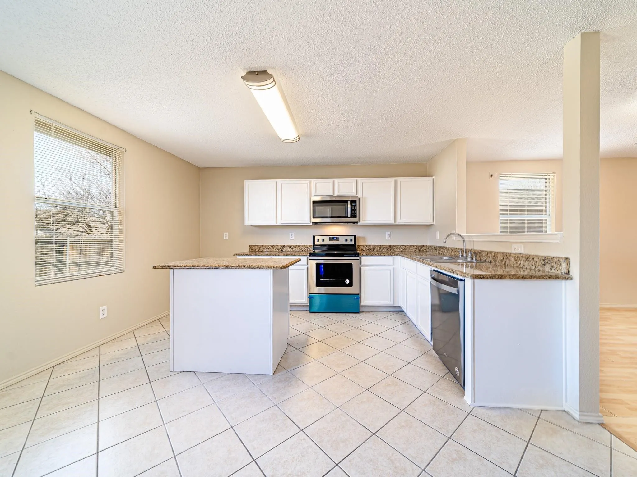 Kitchen featuring white cabinetry, granite-style countertops, stainless steel appliances, and a central island
