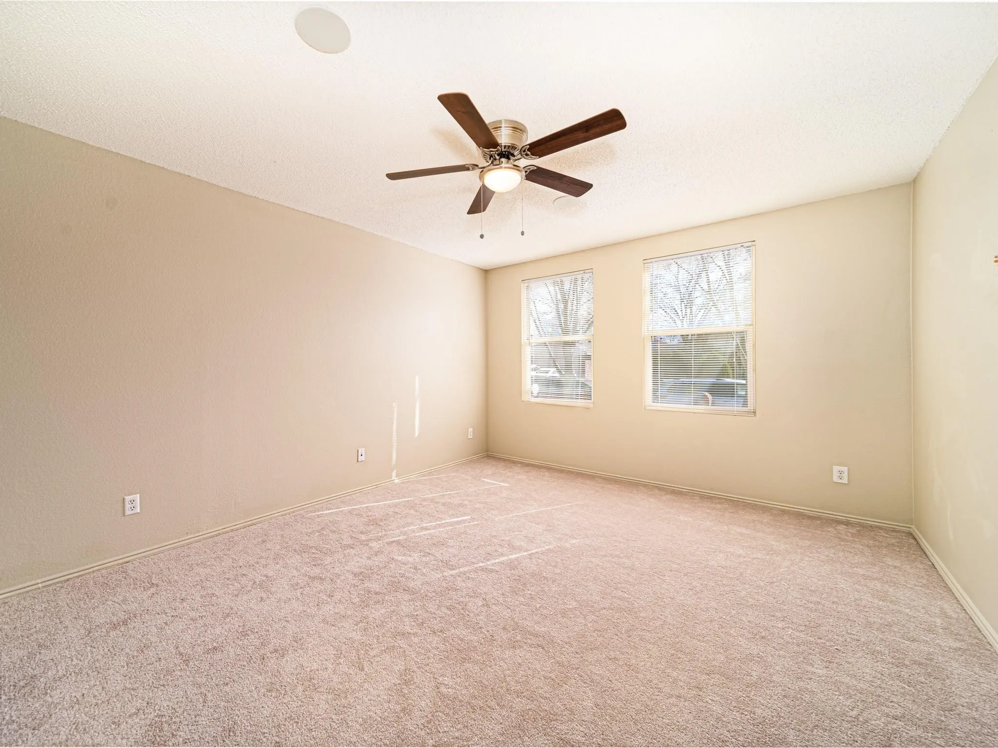 Neutral tone wall finishes, two windows with natural light, textured ceiling, ceiling fan with integrated lighting, and neutral tone carpeting