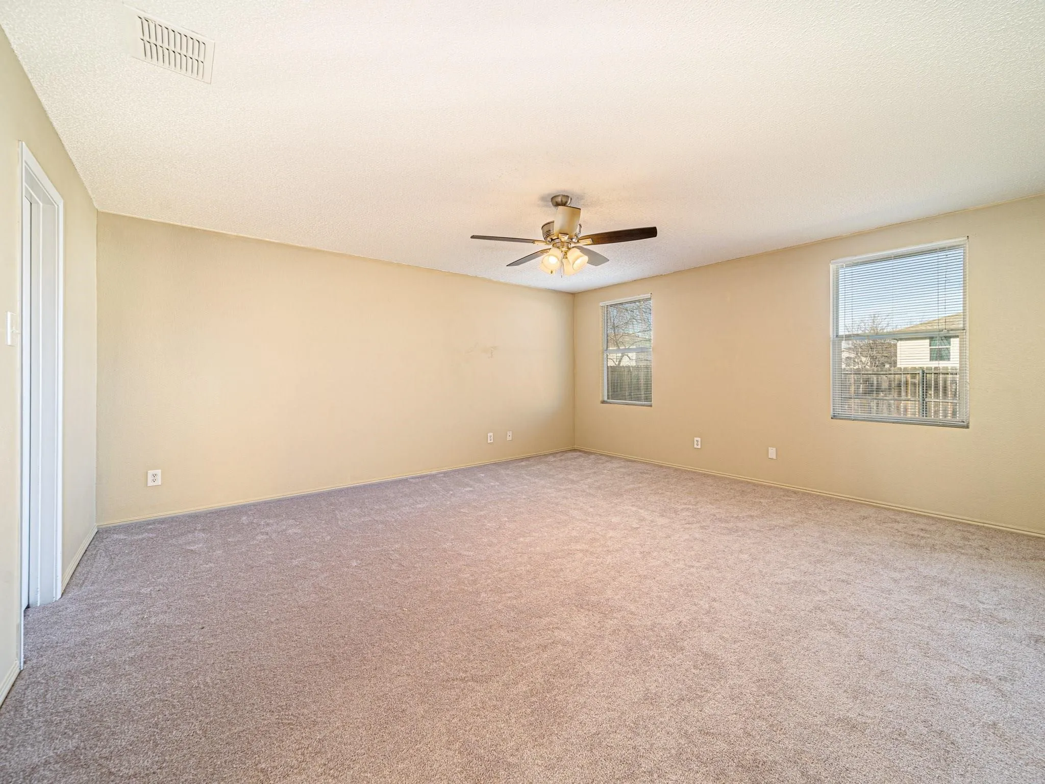 Expansive carpeted room featuring two windows and a ceiling fan with integrated lighting