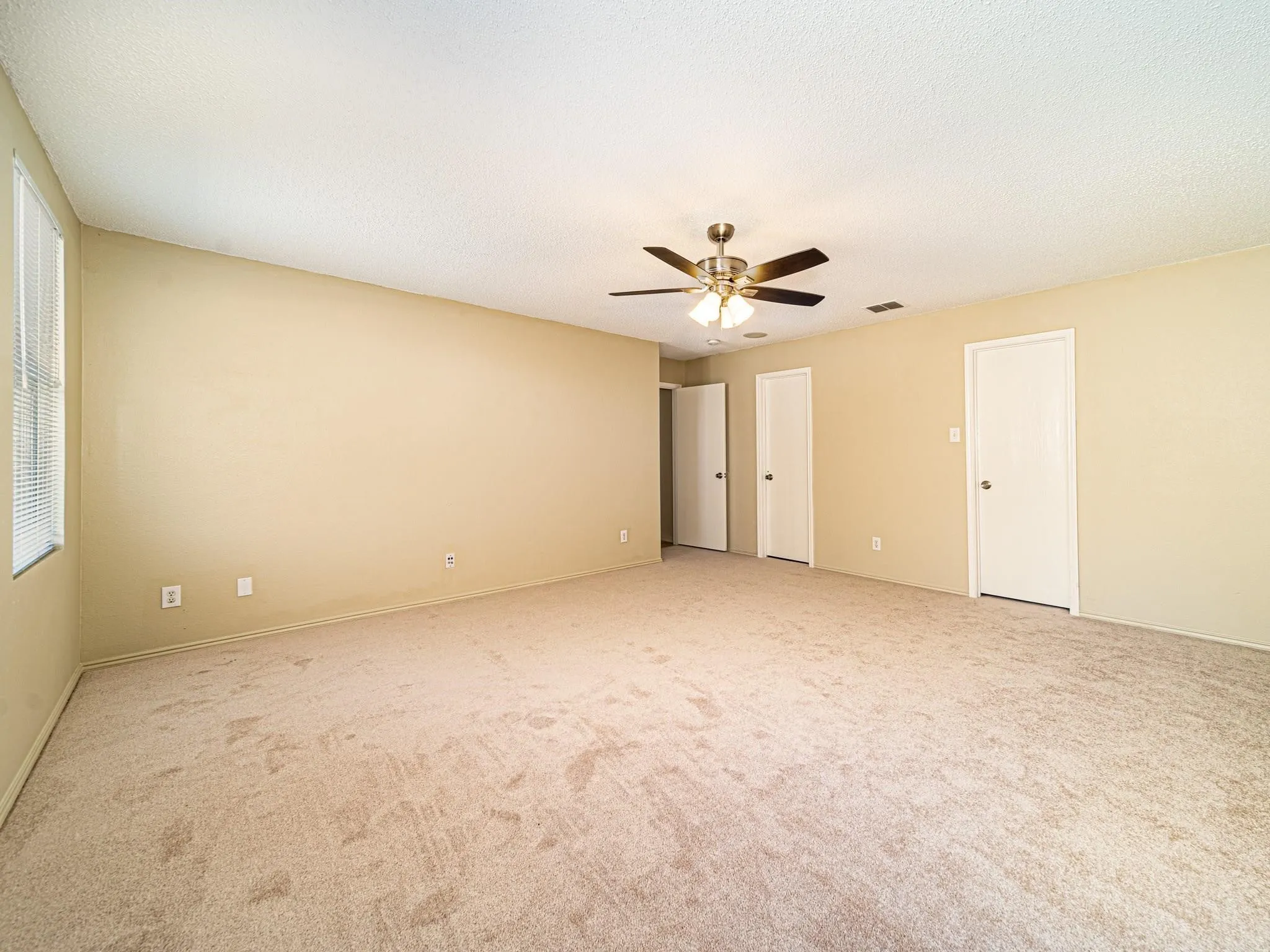 Spacious room featuring neutral carpeting, light-colored walls, and a ceiling fan with integrated lighting