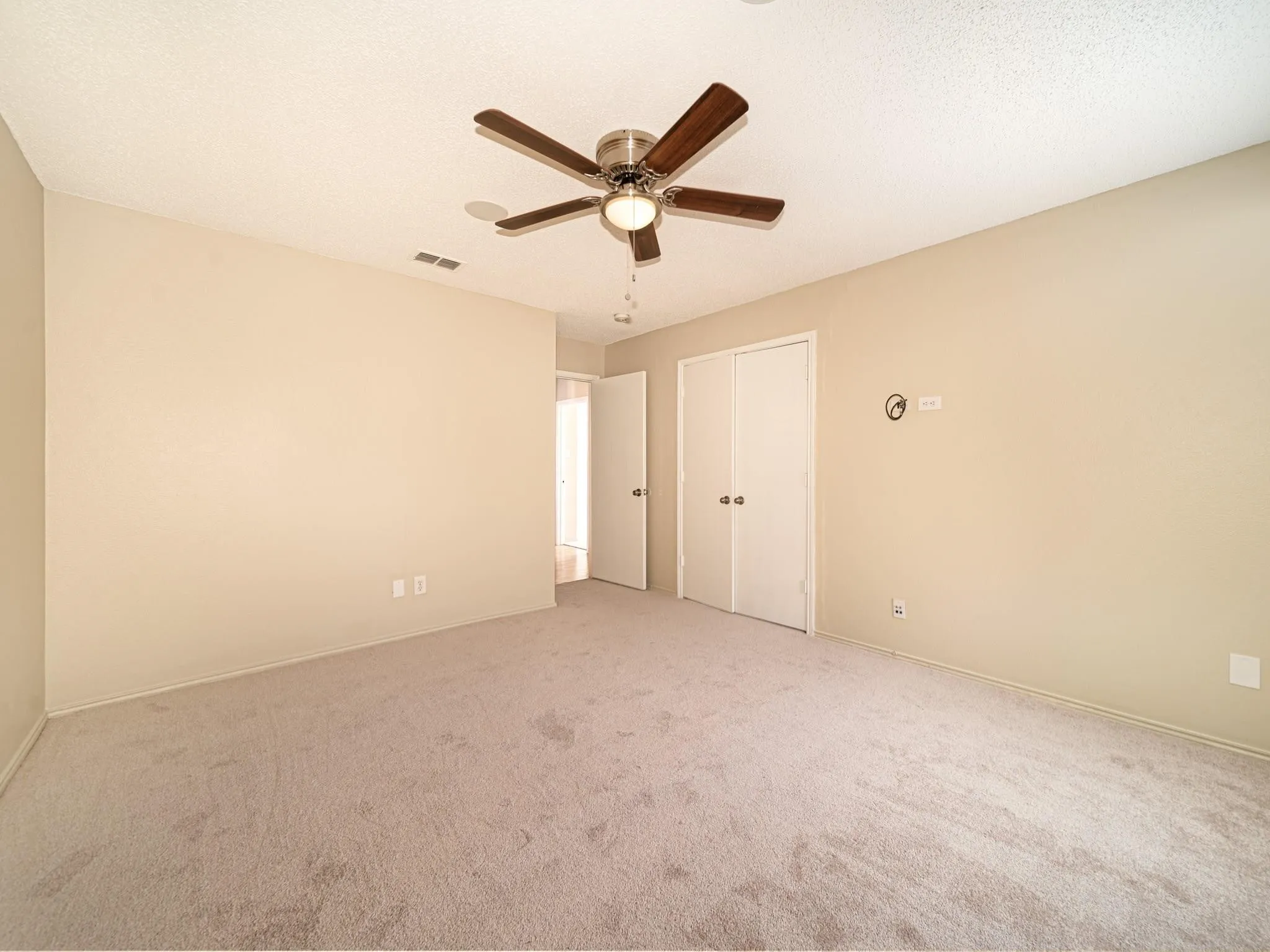 Carpeted flooring, neutral wall tones, ceiling fan with light fixture, and white bi-fold closet doors