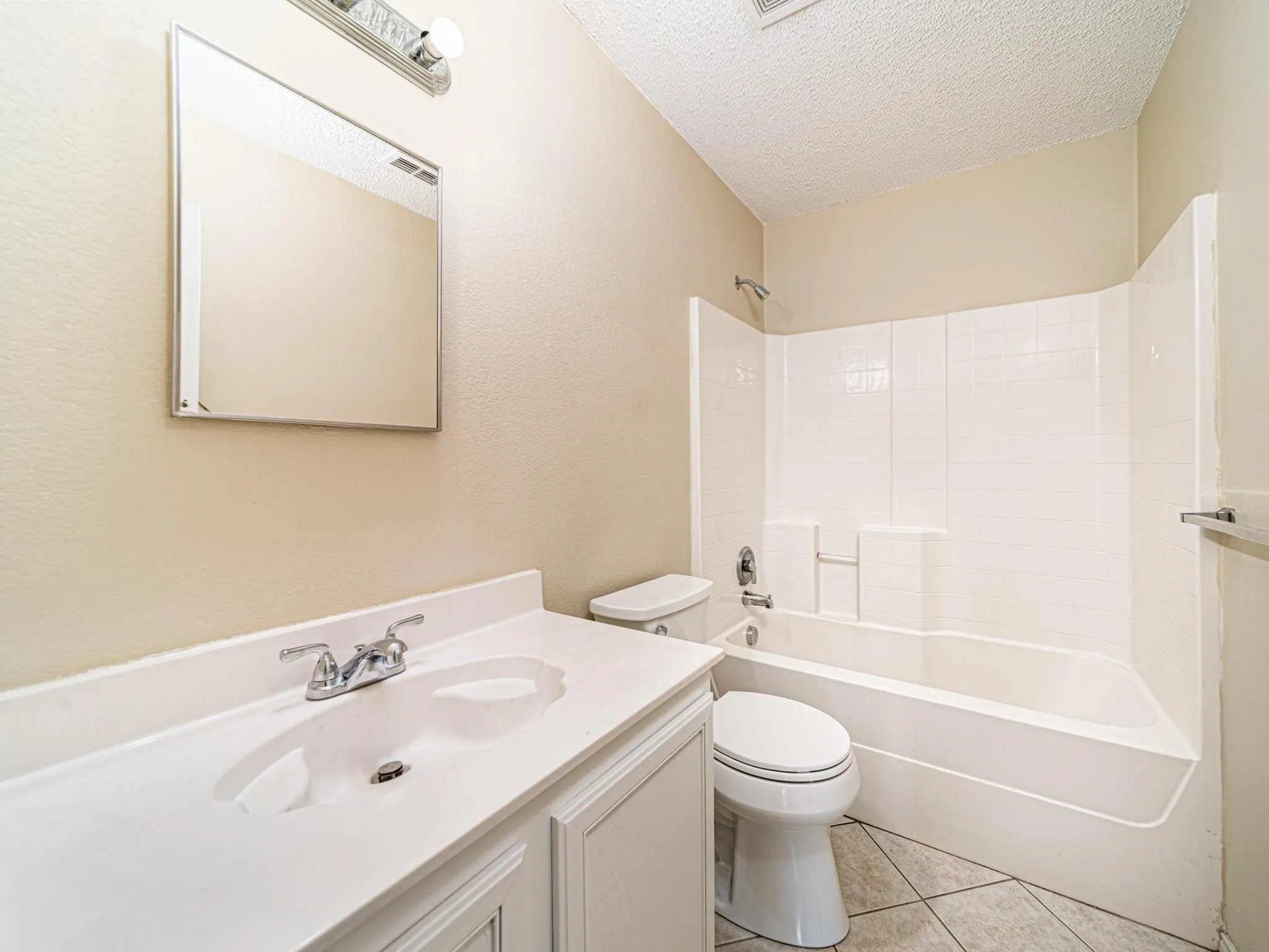 White vanity with an integrated sink, chrome faucet, wall-mounted mirror, and overhead light fixture