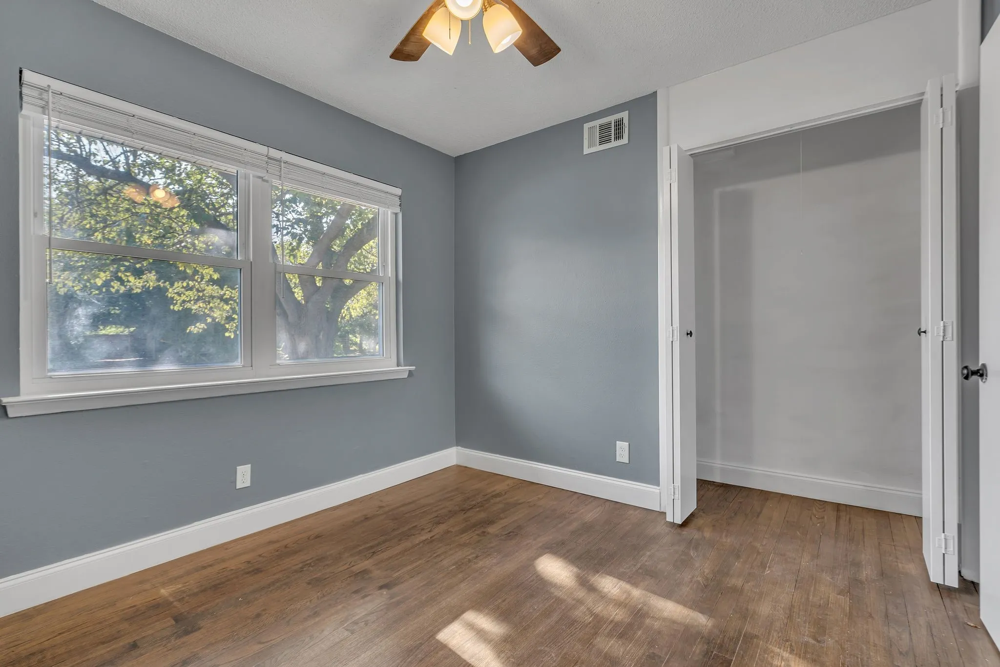 Wood-finish flooring with white trim, a large window with blinds, and an open closet