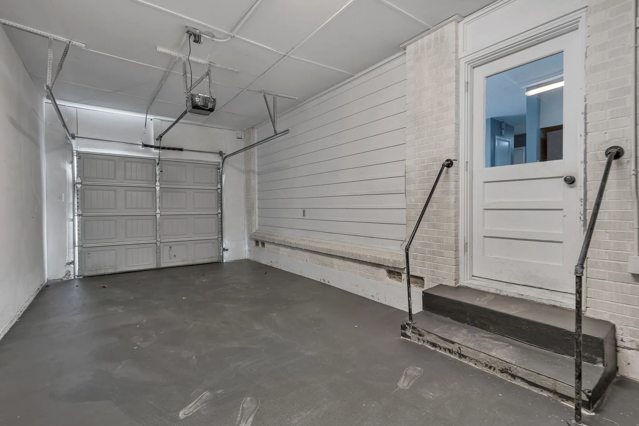 Attached garage featuring an overhead door, smooth concrete flooring, and an additional entry door with a glass panel