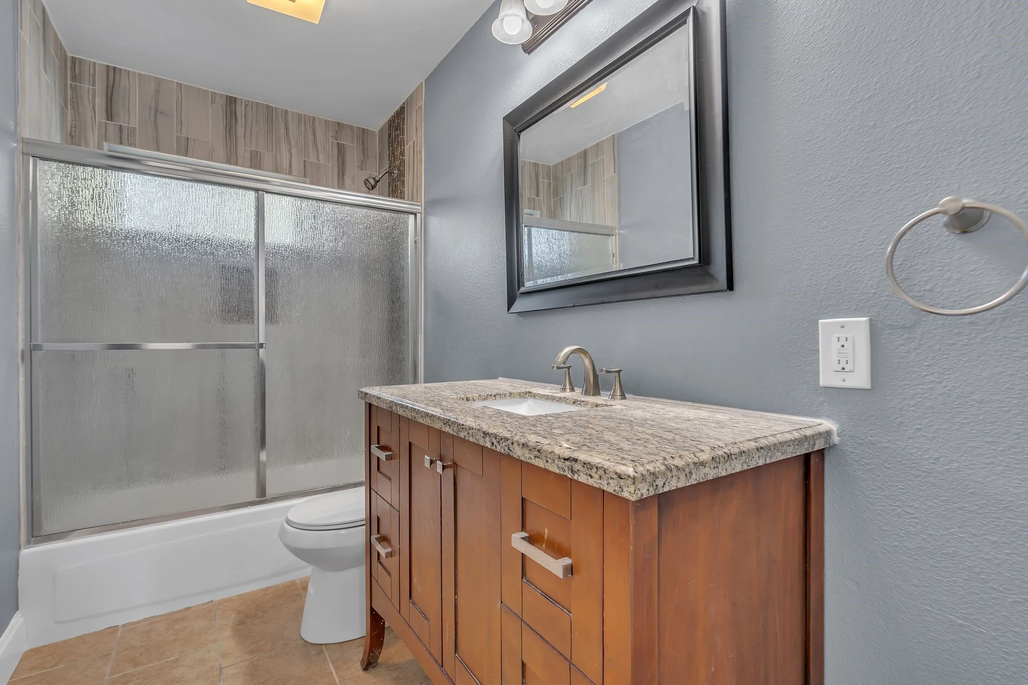 Wood-finish vanity with a stone countertop, an undermount sink, and a framed mirror