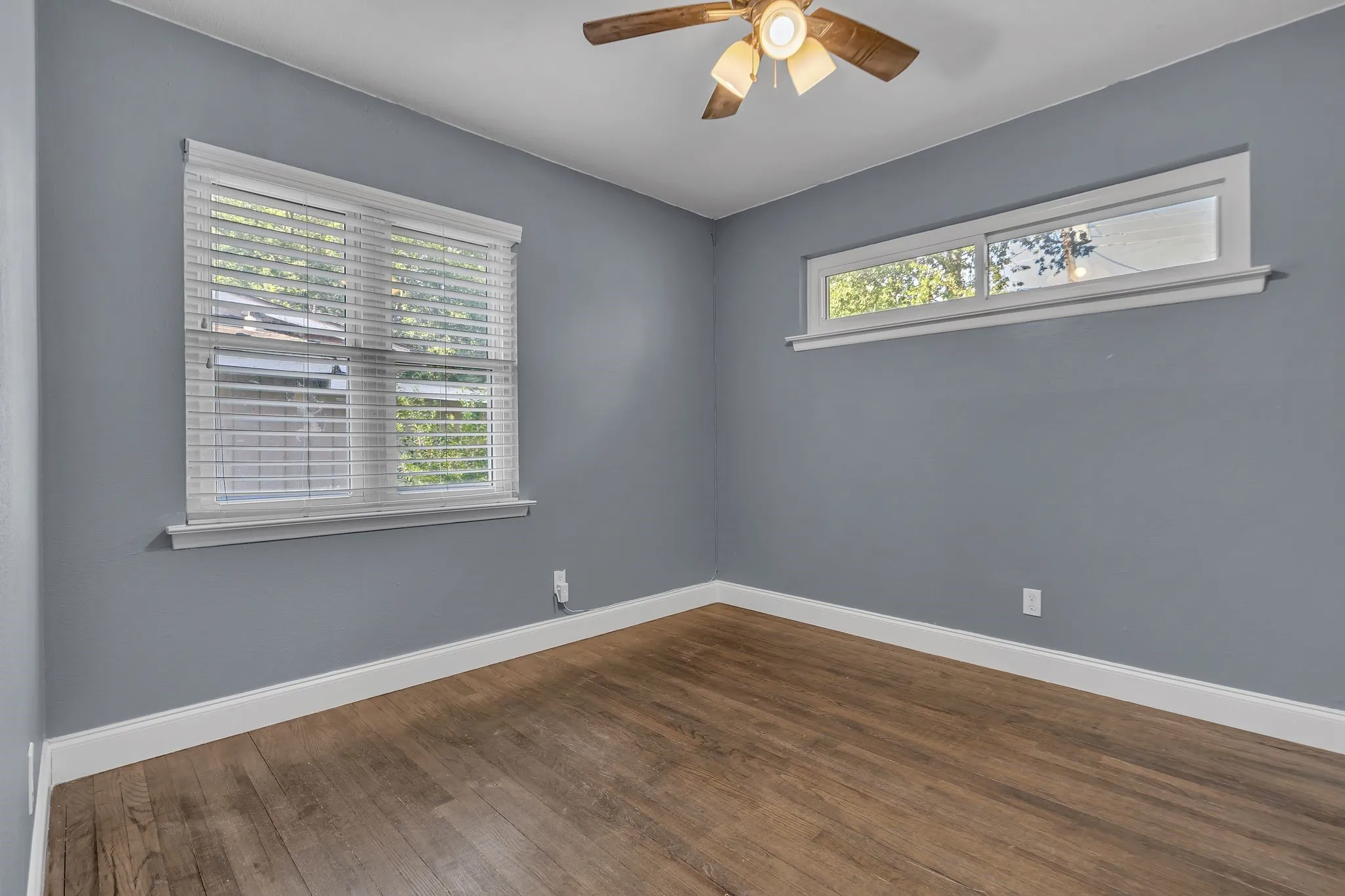 Wood-finish flooring, two distinct window styles, white trim, and a ceiling fan with integrated lighting