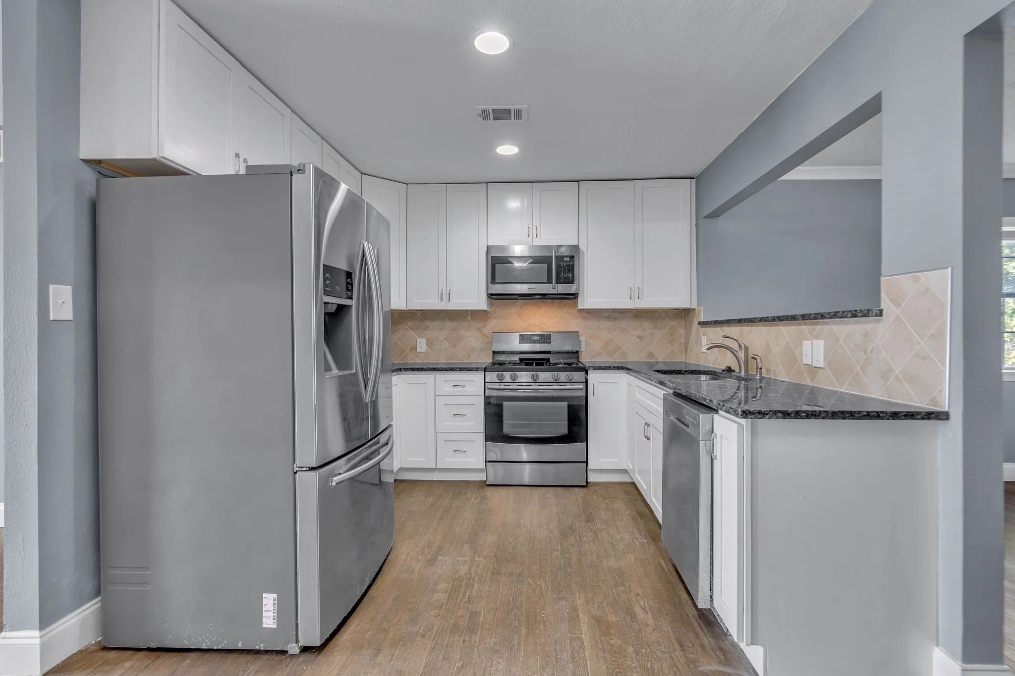 Kitchen featuring stainless steel appliances, dark countertops, white cabinetry, tile backsplash, and wood-finish flooring