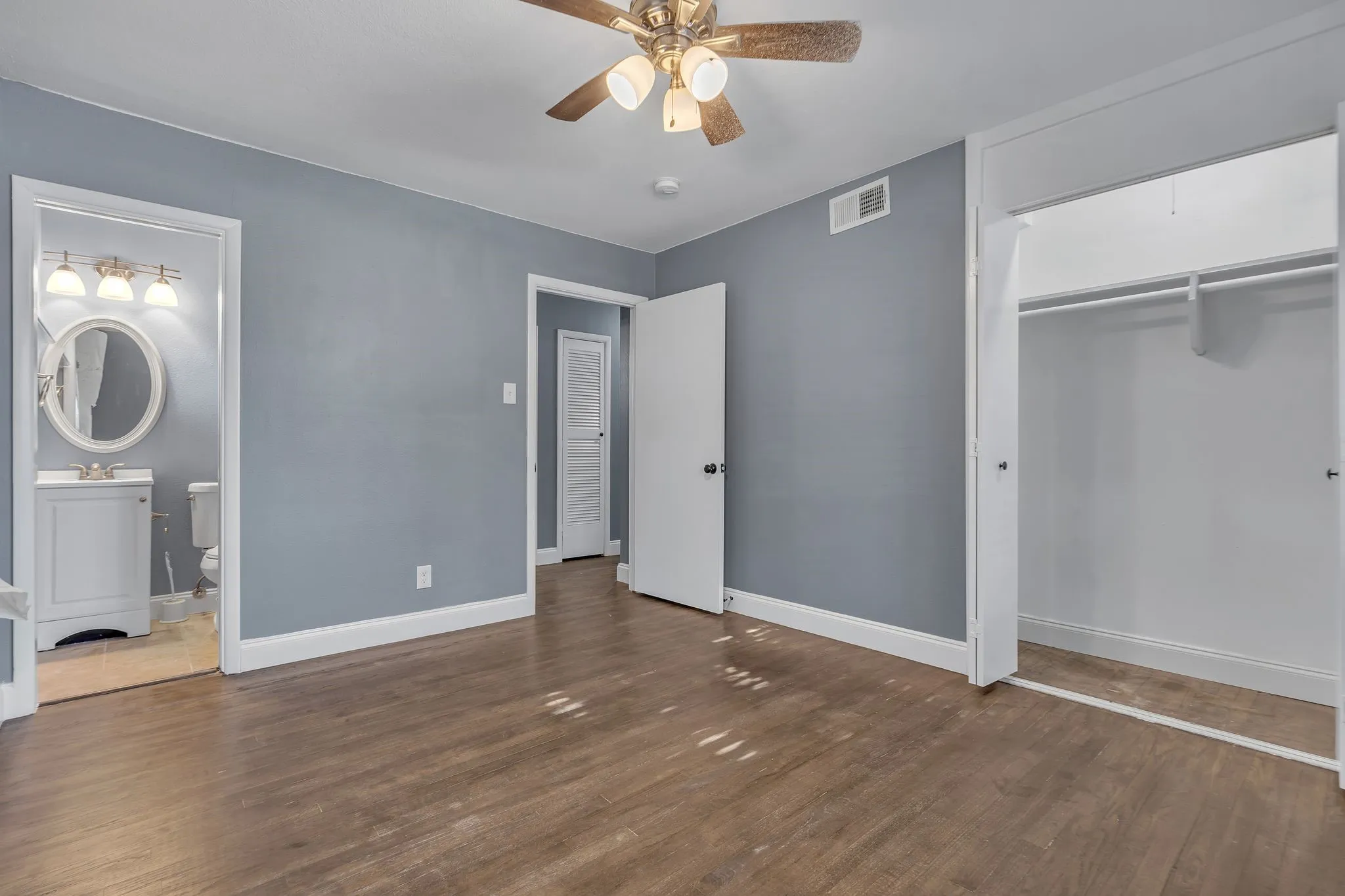 Wood-finish flooring, ceiling fan with integrated lighting, and an open closet with shelving