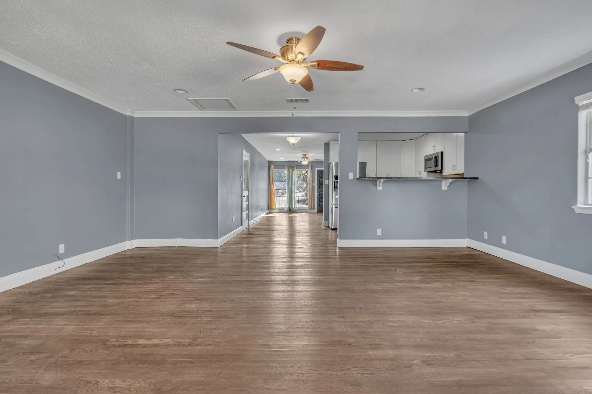 Wood-finish flooring throughout, ceiling fan with integrated lighting, crown molding, and a pass-through counter to the kitchen featuring a built-in microwave