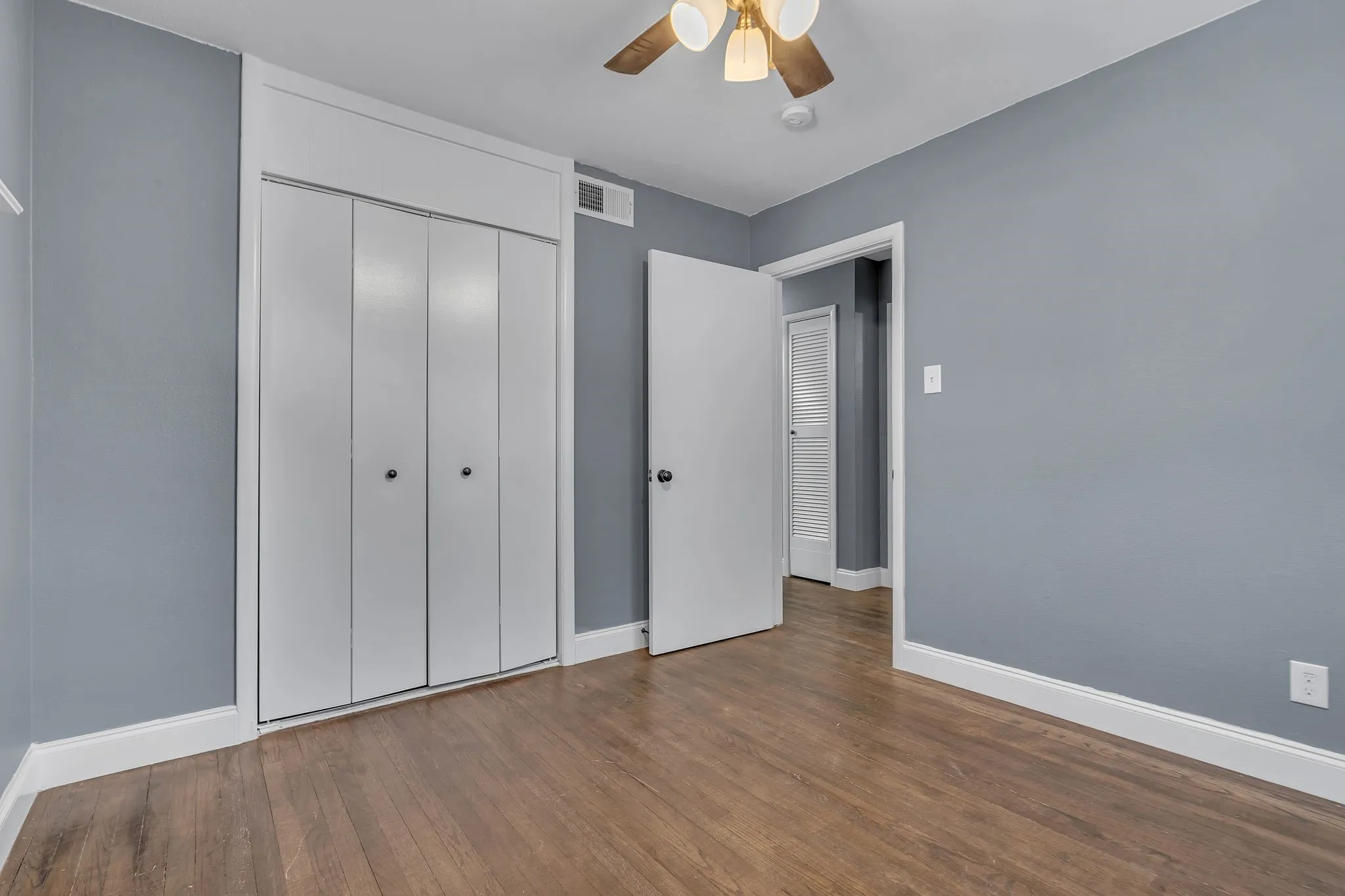 Wood-finish flooring, white bi-fold closet doors, ceiling fan with integrated lighting, white trim