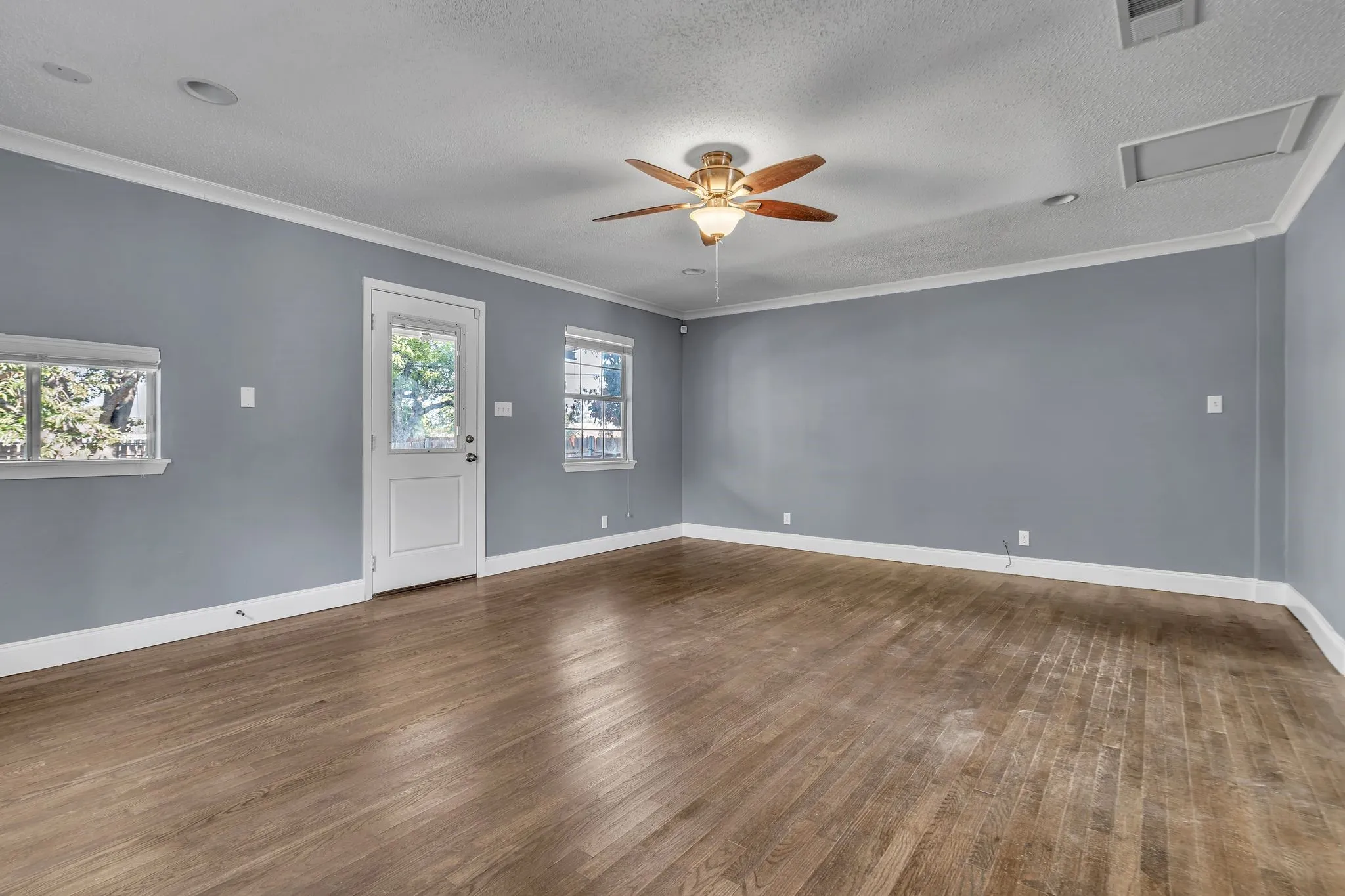 Hardwood flooring, painted walls, ceiling fan with integrated lighting, multiple windows, and a glass-paneled door