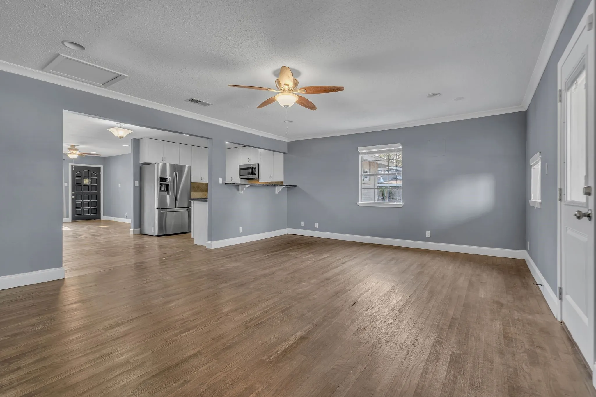 Spacious living area featuring wood-finish flooring, a ceiling fan, and crown molding