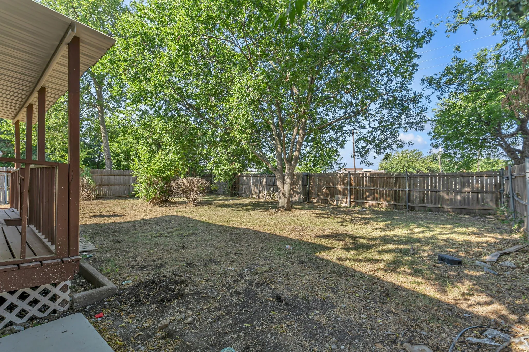 Expansive backyard featuring mature trees, partial wood fencing, and a covered porch with wood railing