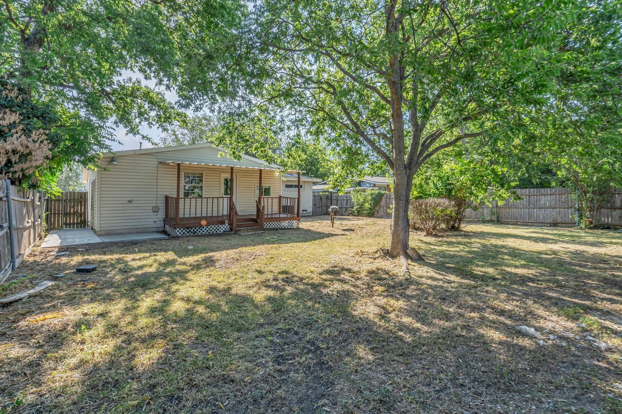 Expansive yard featuring mature trees, a covered porch with railings, horizontal siding, and a privacy fence