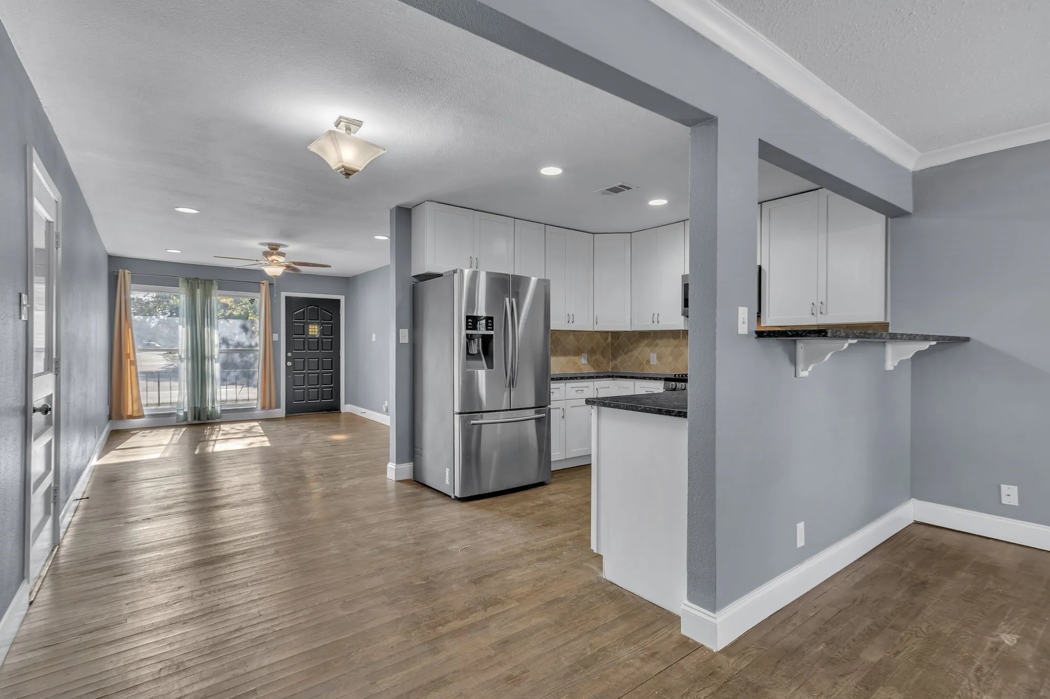 Kitchen with white cabinetry, stainless steel refrigerator, dark countertops, and a built-in breakfast bar