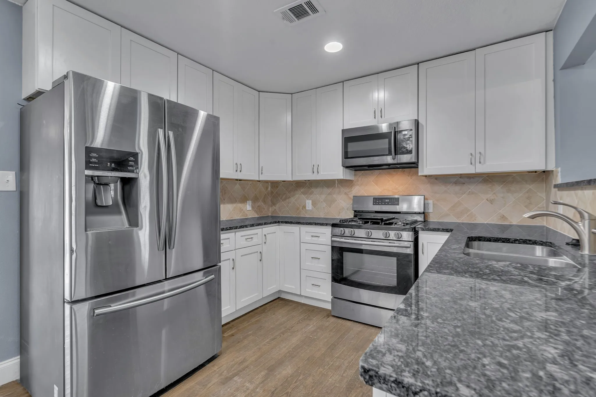 Kitchen featuring white shaker cabinetry, stainless steel appliances, dark stone countertops, tile backsplash, and wood-finish flooring