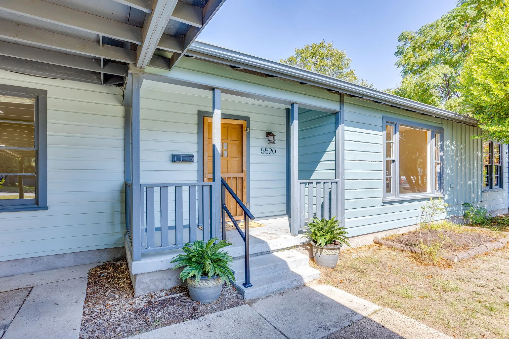 Covered front porch with light blue siding, gray trim, and natural wood front door