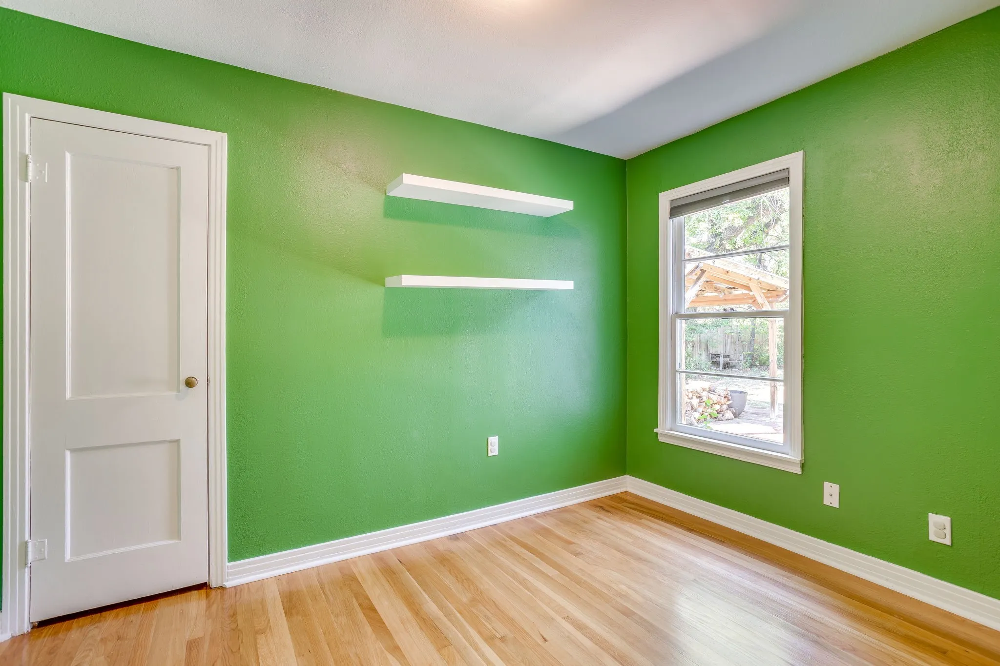 Hardwood flooring with white trim, two floating wall shelves, and a double-hung window with a white frame