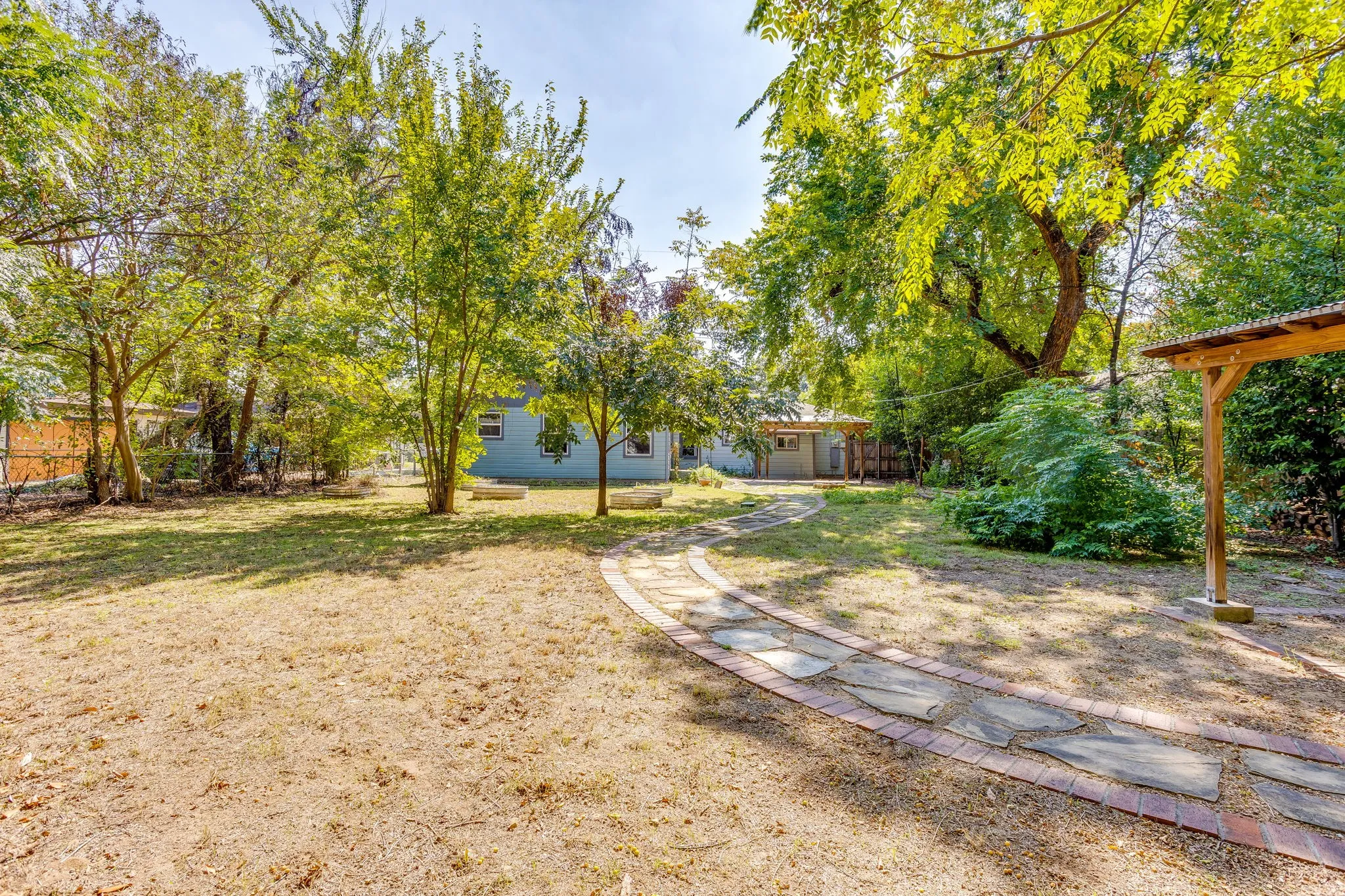 Expansive yard featuring a stone and brick pathway, mature trees, and a wooden pergola structure