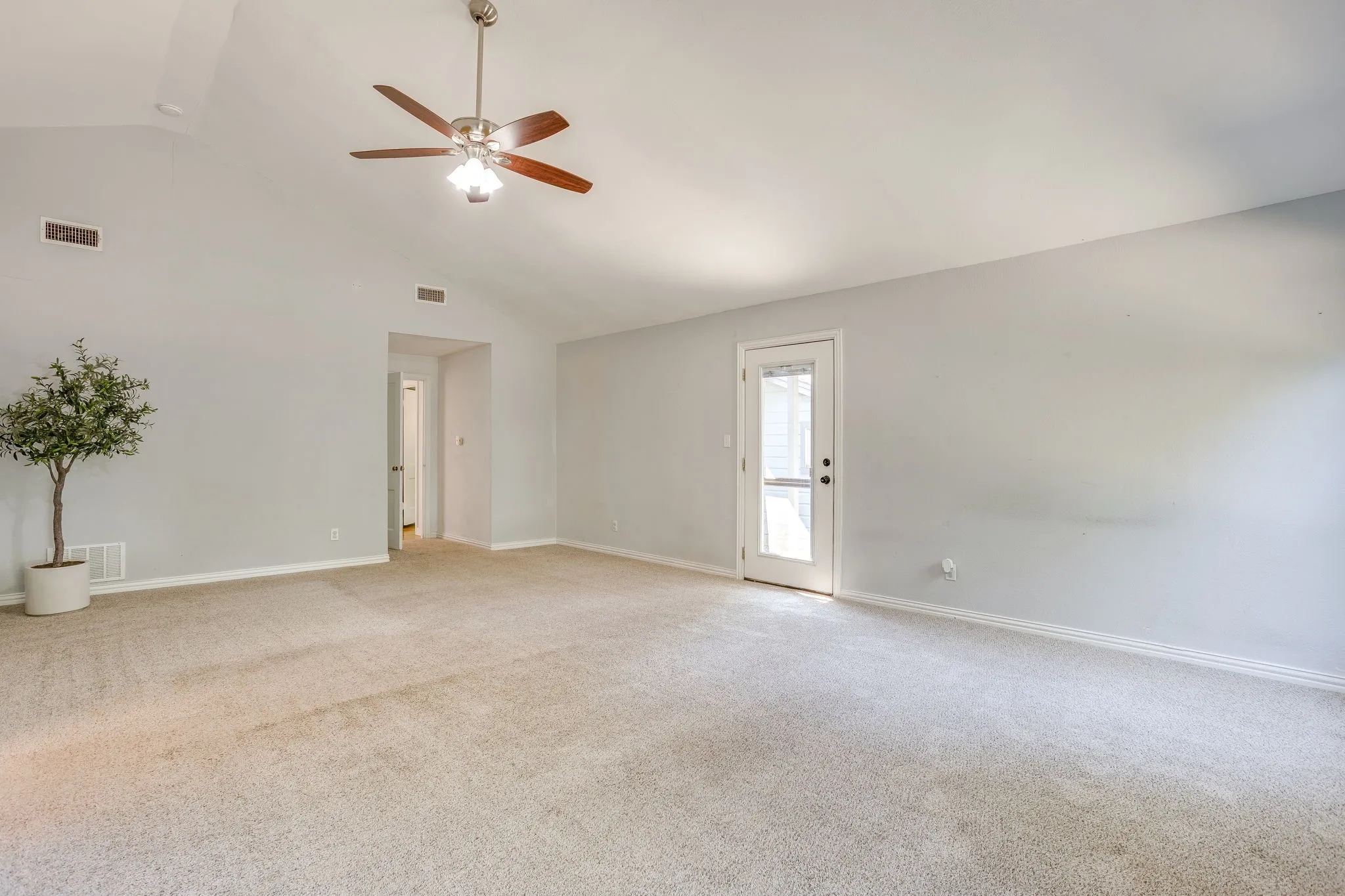 Vaulted ceiling with a wood-finish ceiling fan, neutral carpet, and a glass-paneled exterior door