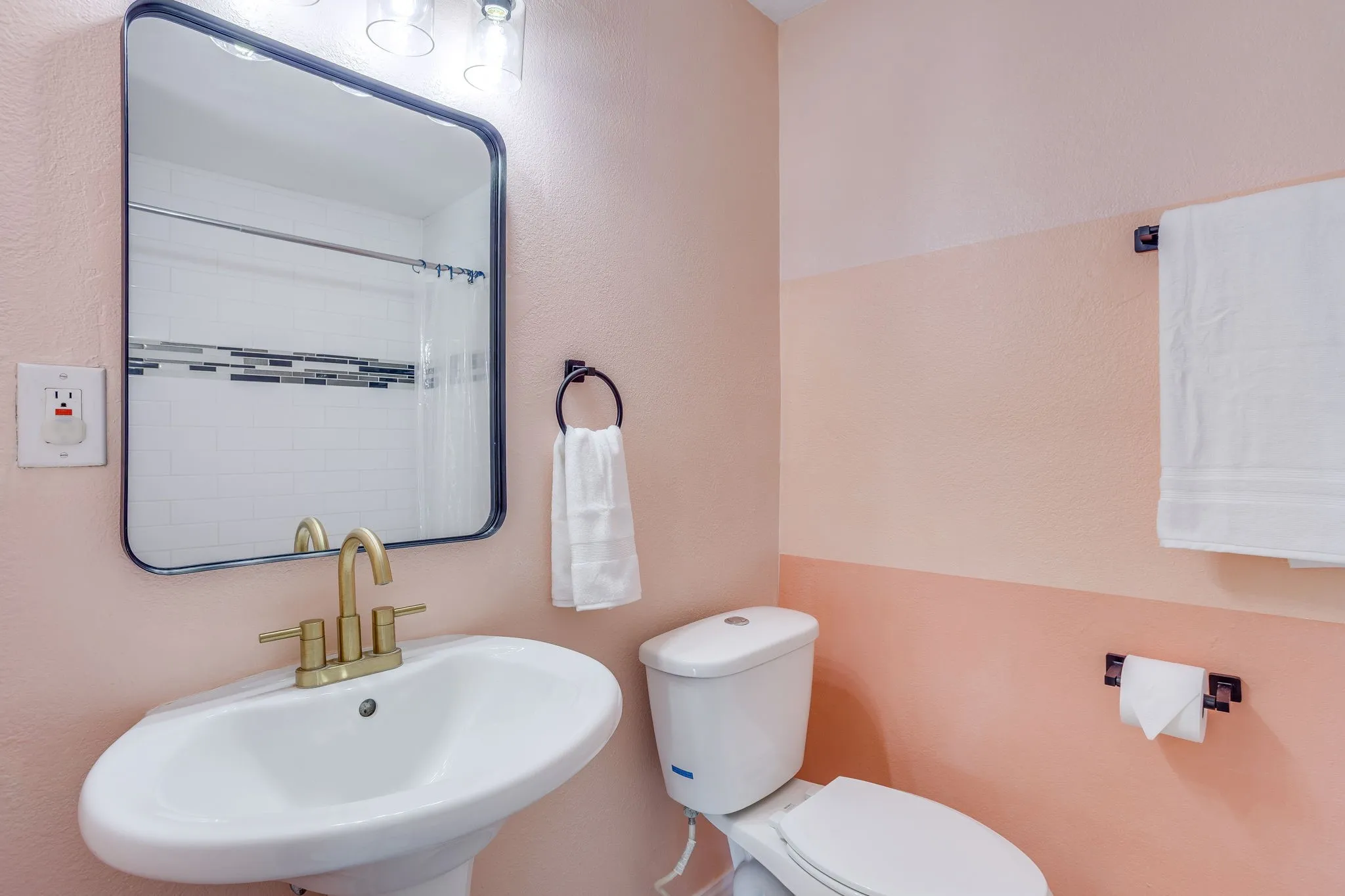 Pedestal sink with brass-finish faucet, rectangular framed mirror, and tiled shower surround with accent band