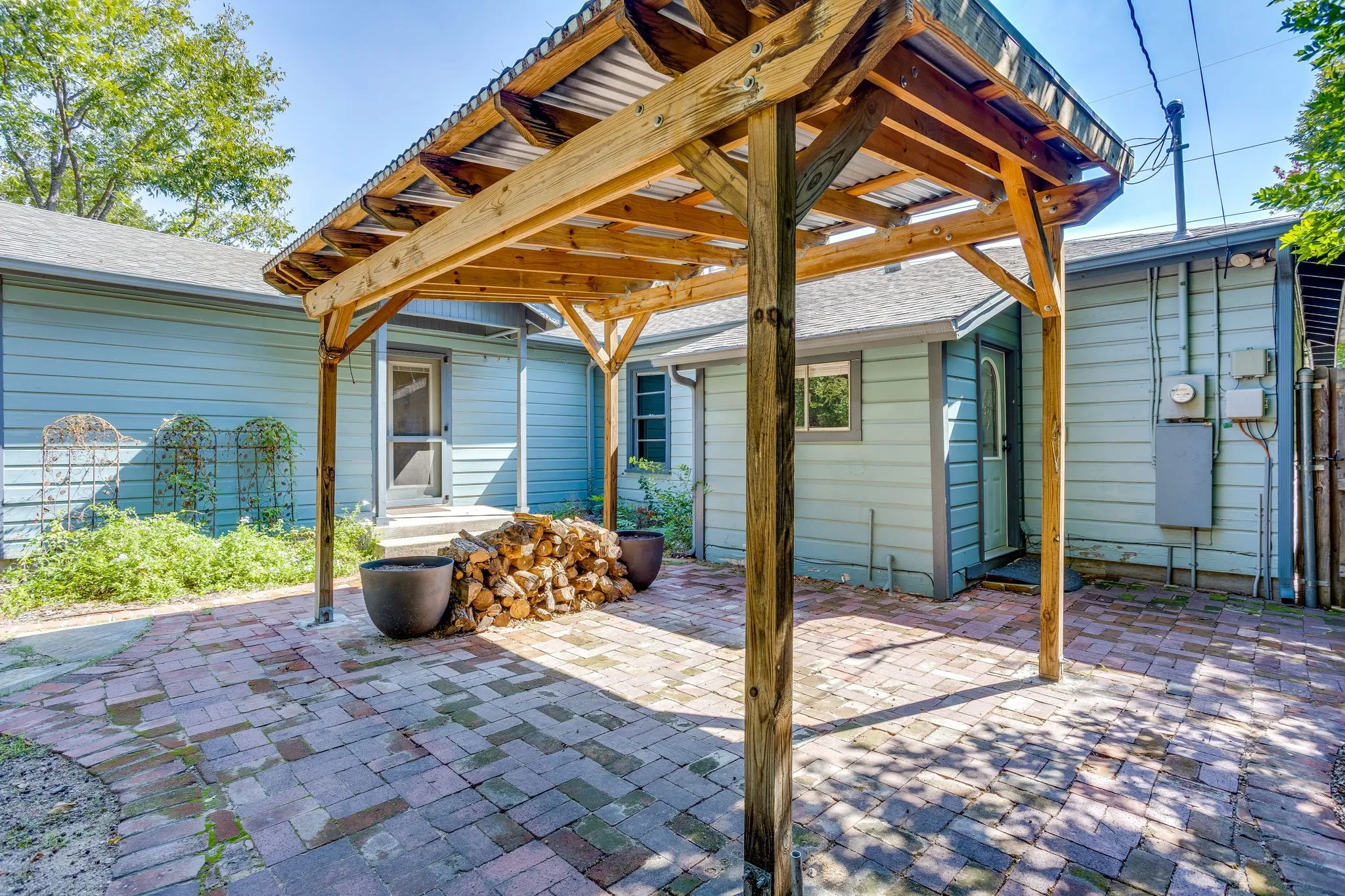 Brick paver patio with a wood pergola featuring a corrugated metal roof