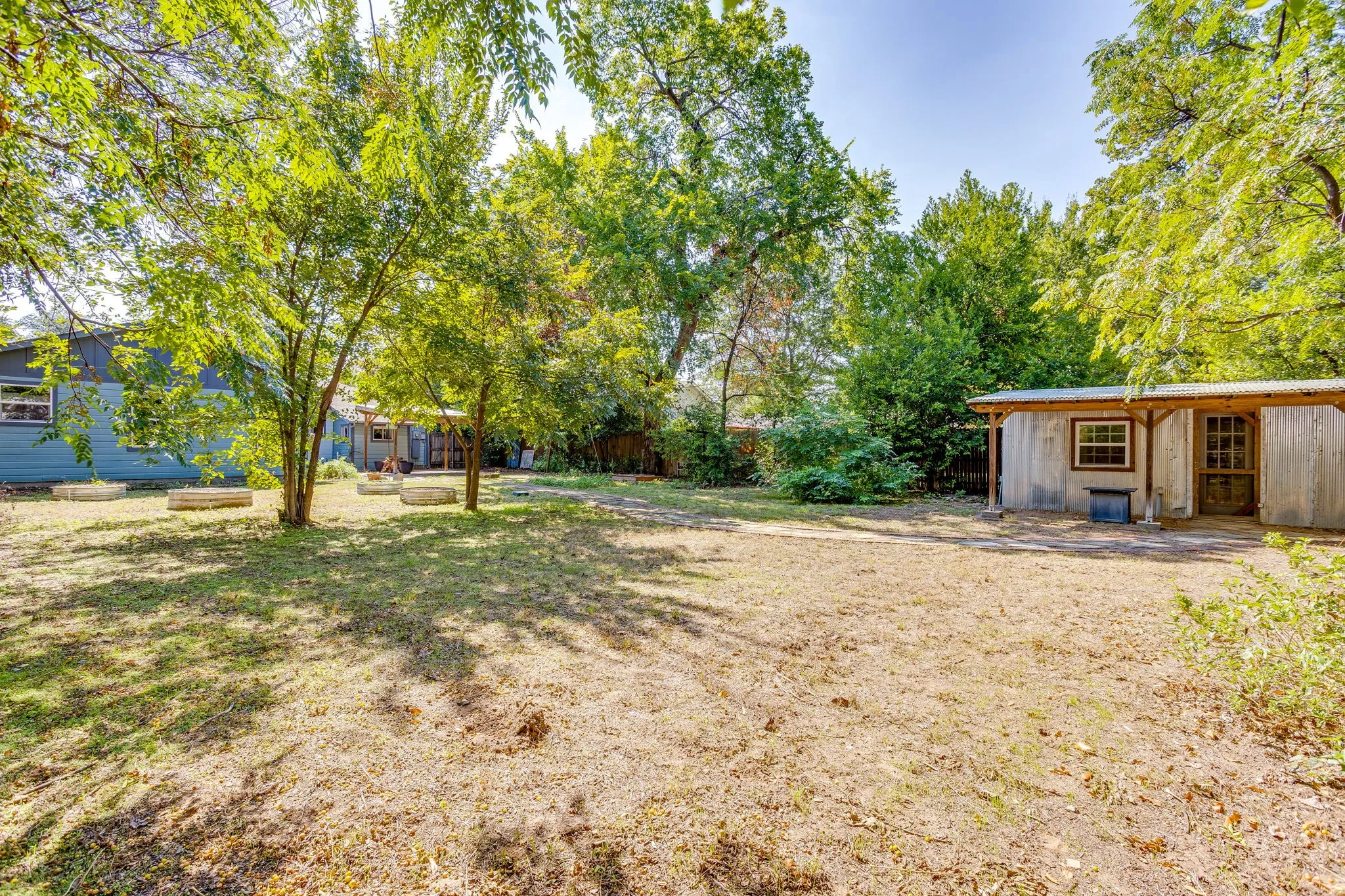 Expansive outdoor space featuring mature trees, a detached storage structure with a covered porch, and raised garden beds