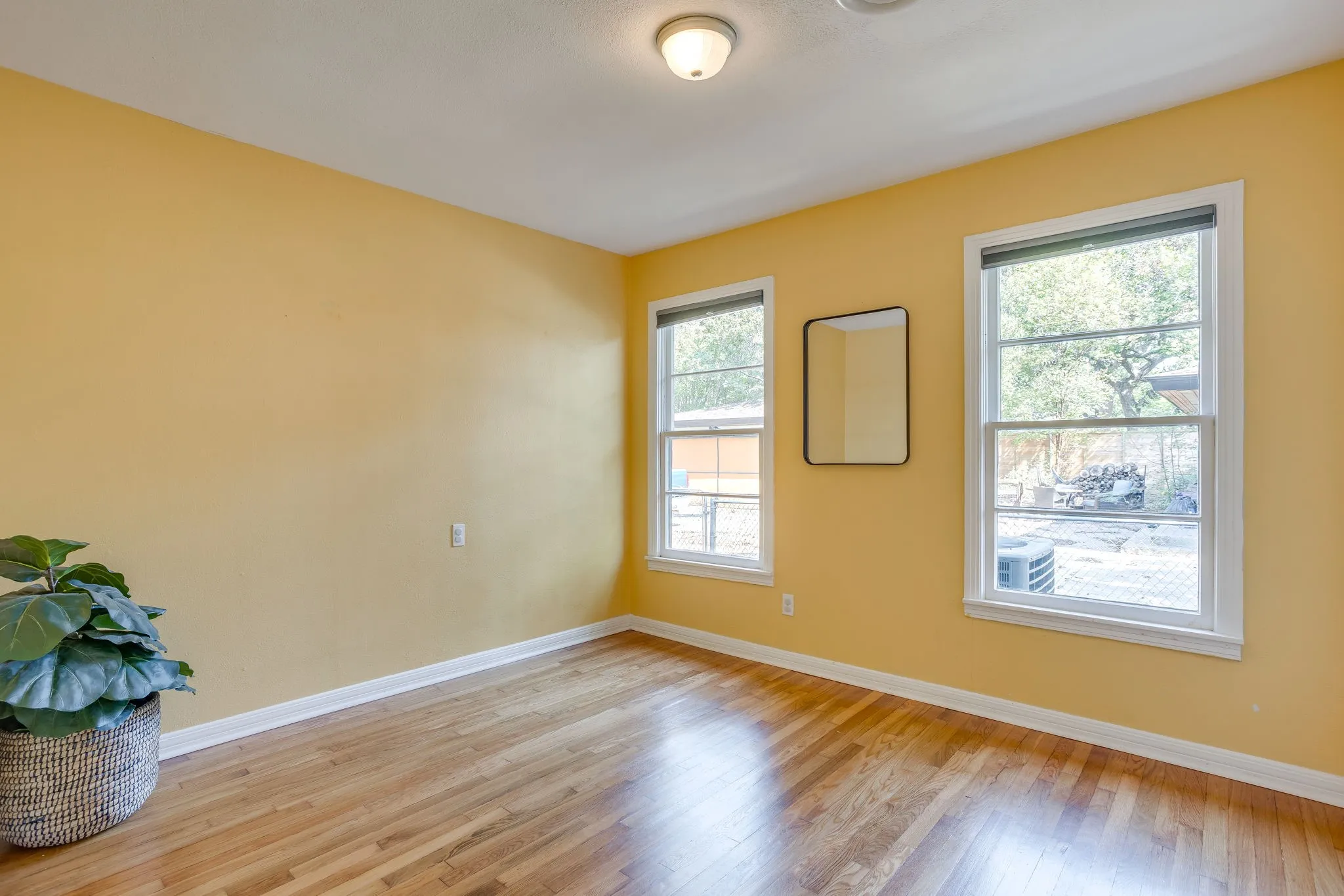 Warm yellow walls, wood-finish flooring, white trim, and two double-hung windows